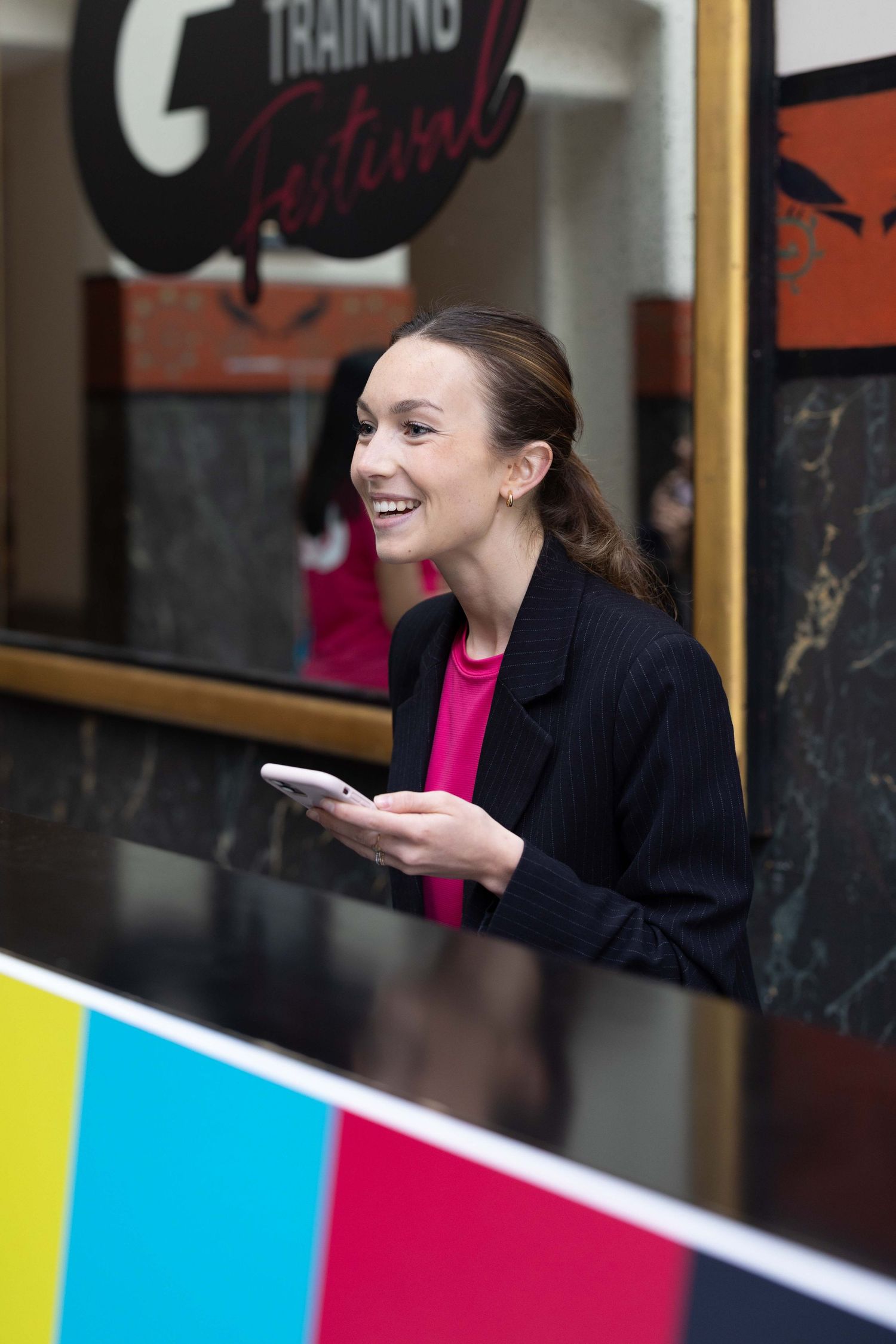 Person in business attire smiles while checking phone at colorful event space.