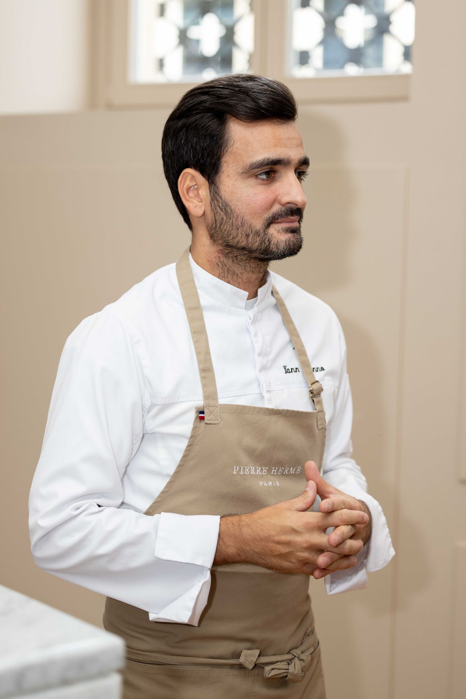 Person in white chef coat and tan apron during professional event.