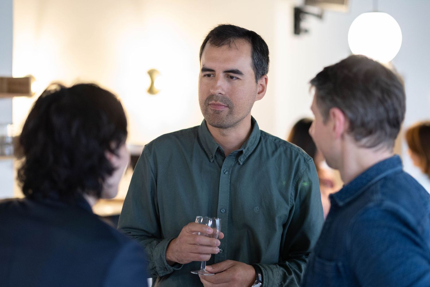 Three people engaged in conversation at a casual indoor gathering.