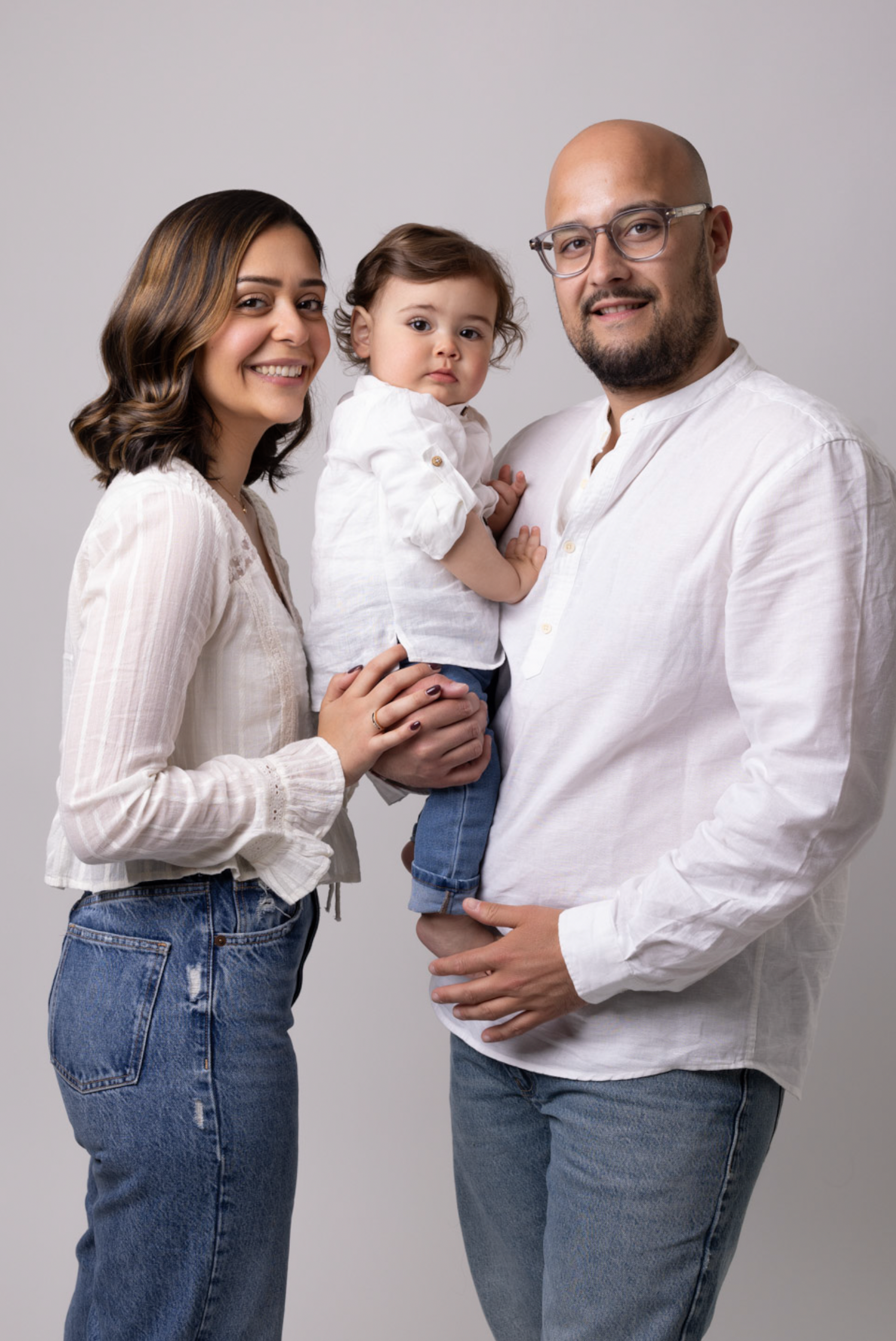 A series of four candid family portraits showing joyful moments in matching white shirts and blue jeans against a gray backdrop.