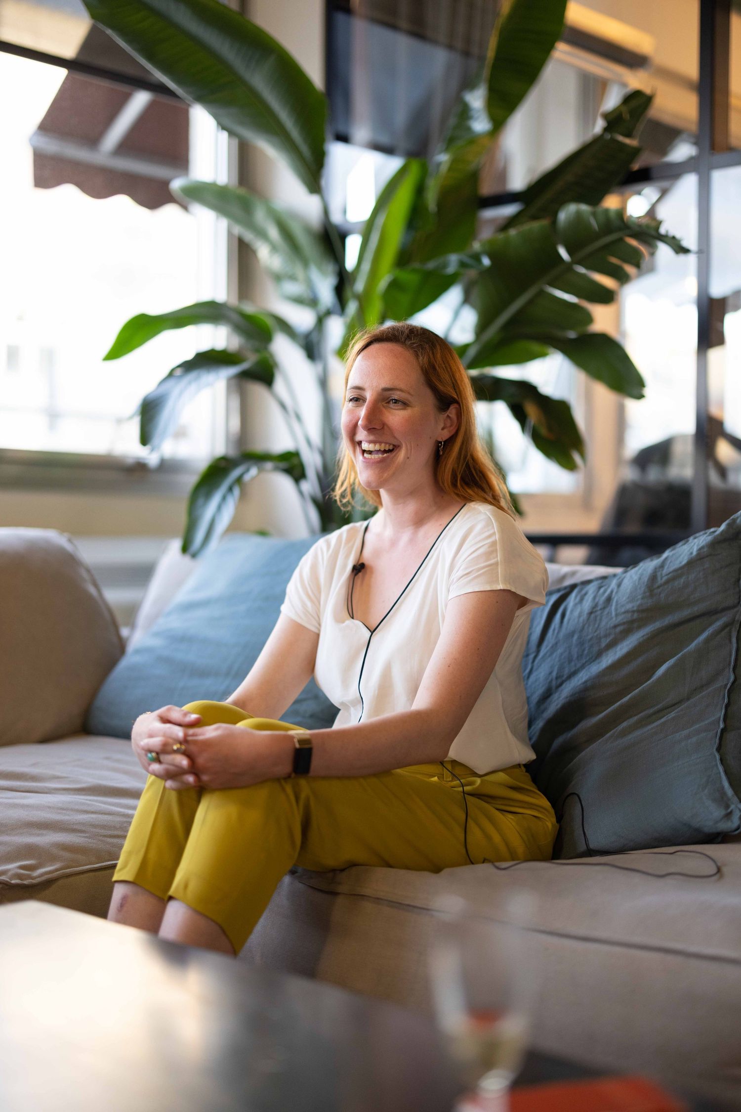 Person relaxing on a grey couch near a large indoor plant.