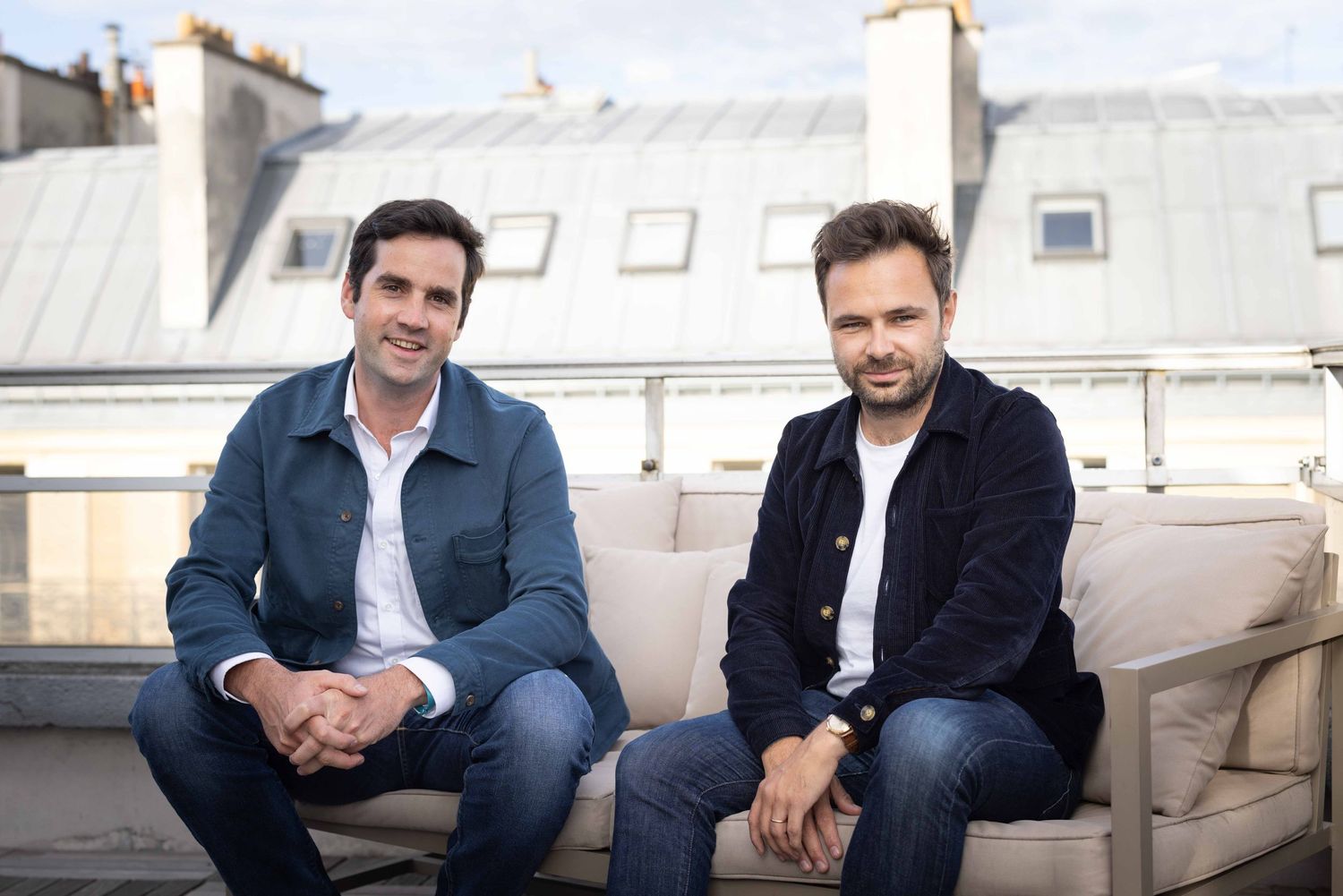 Two people sitting on outdoor furniture on a Parisian rooftop terrace.