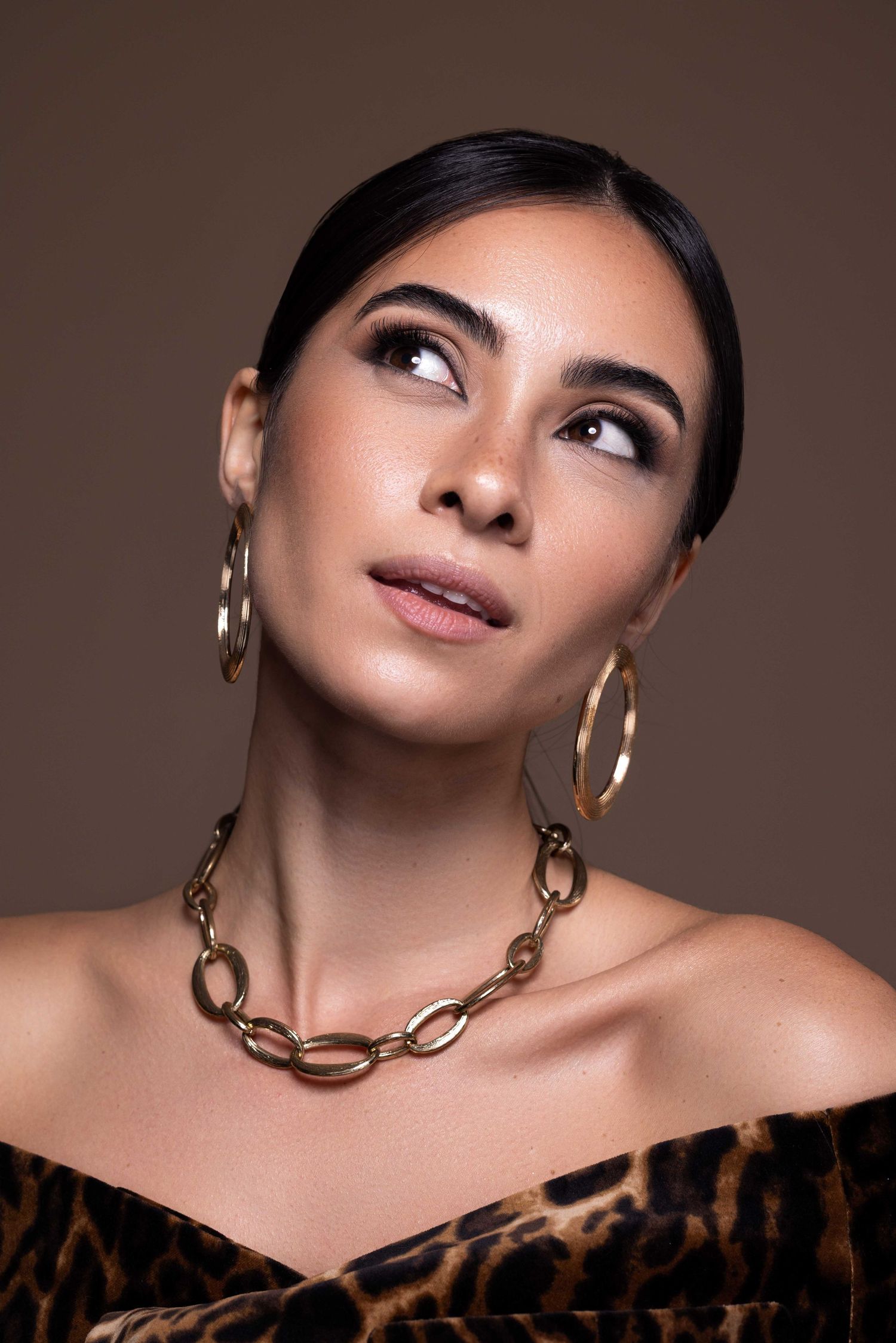 Portrait glamour avec collier en chaîne en or et boucles d'oreilles créoles avec regard vers le haut.