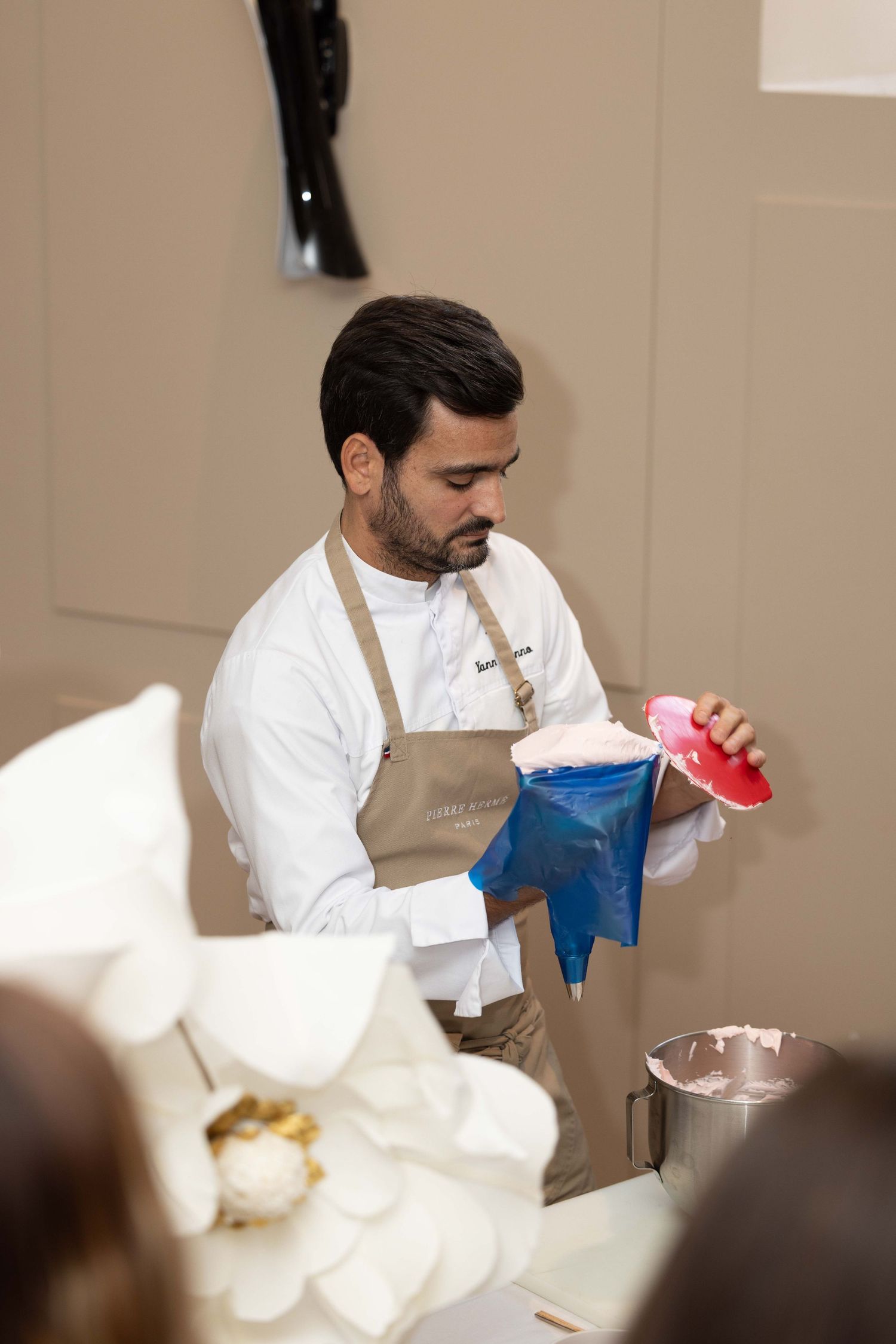 Chef in white coat and beige apron handling blue and red containers during food preparation.