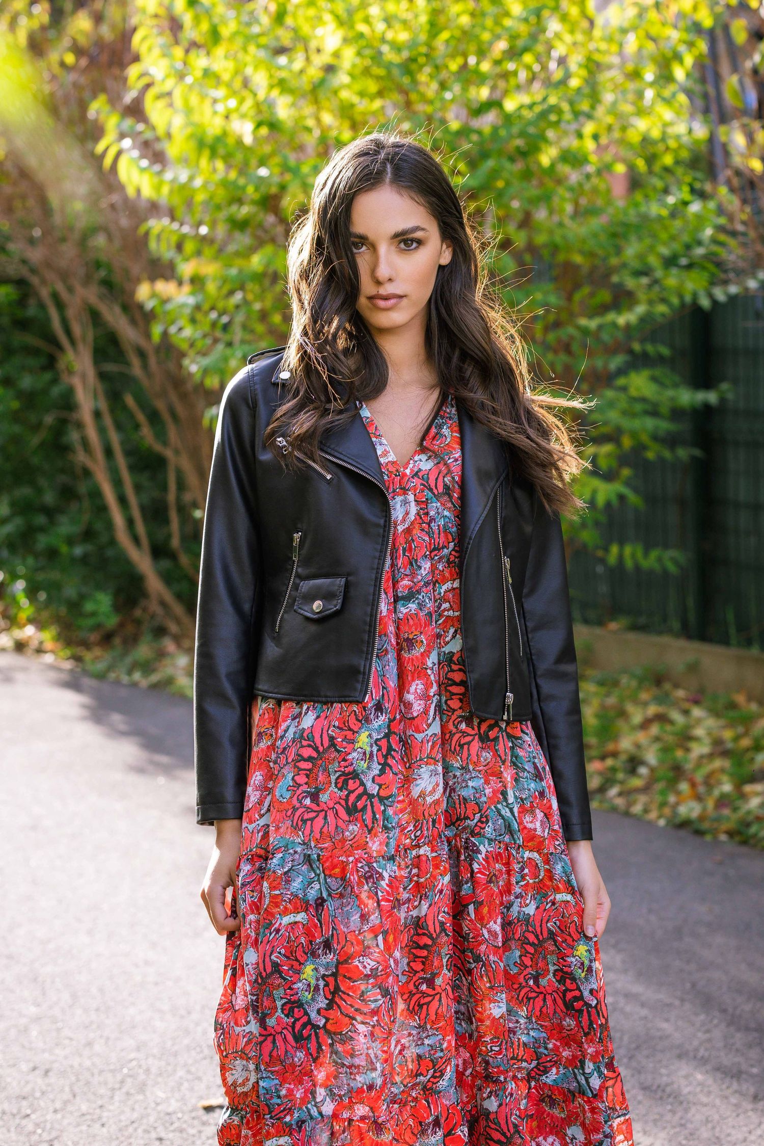 Photographie de mode mettant en vedette une robe fleurie et une veste en cuir dans un cadre de jardin extérieur.