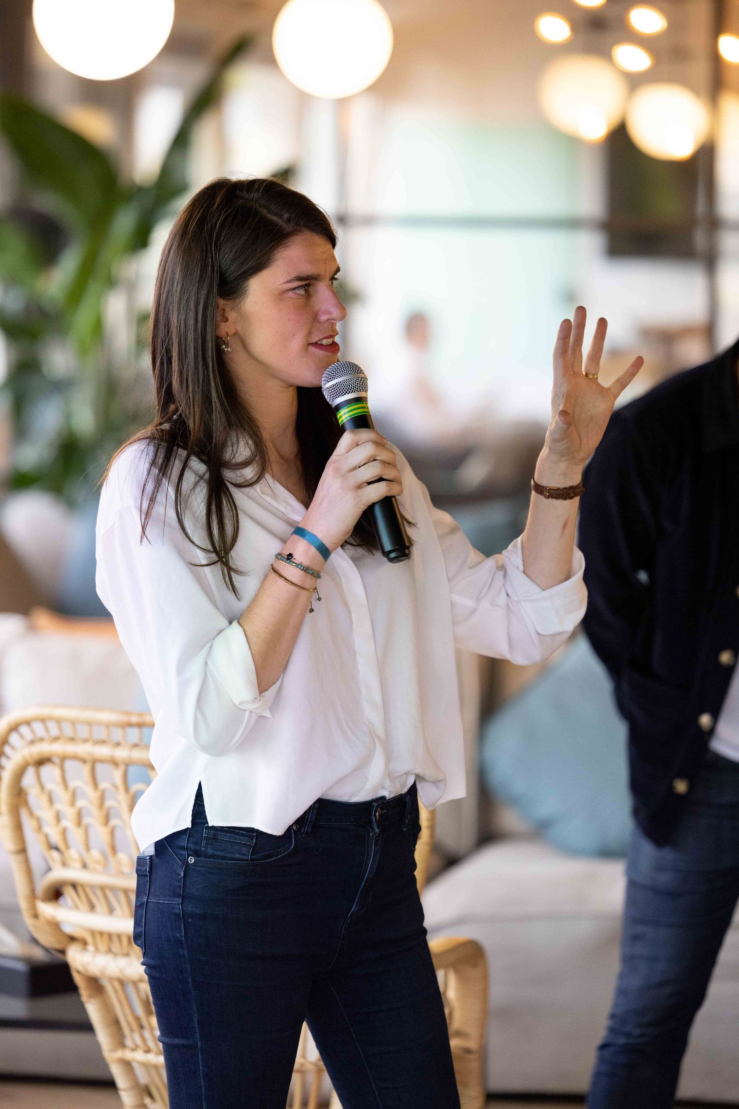 A speaker in a white shirt and dark pants gestures while presenting with a microphone.