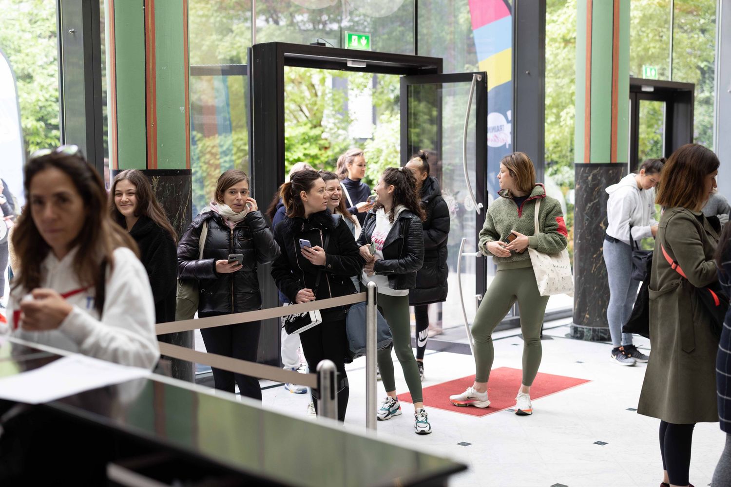 Attendees wait in line at security check point inside modern venue entrance.