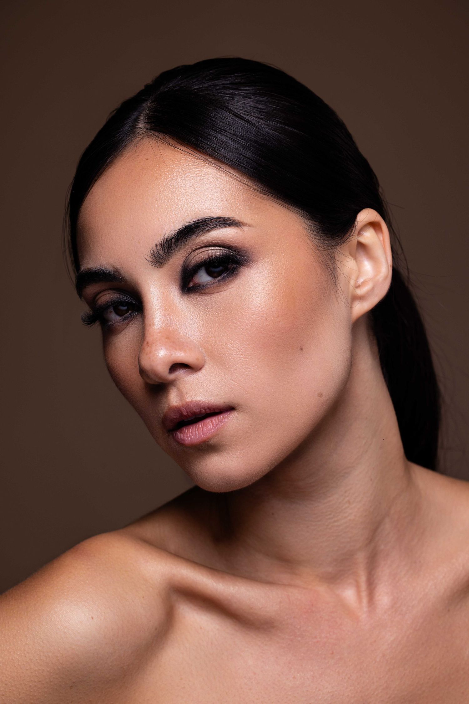 Beauté élégante photographiée avec un maquillage des yeux dramatique et des cheveux lisses sur fond marron.
