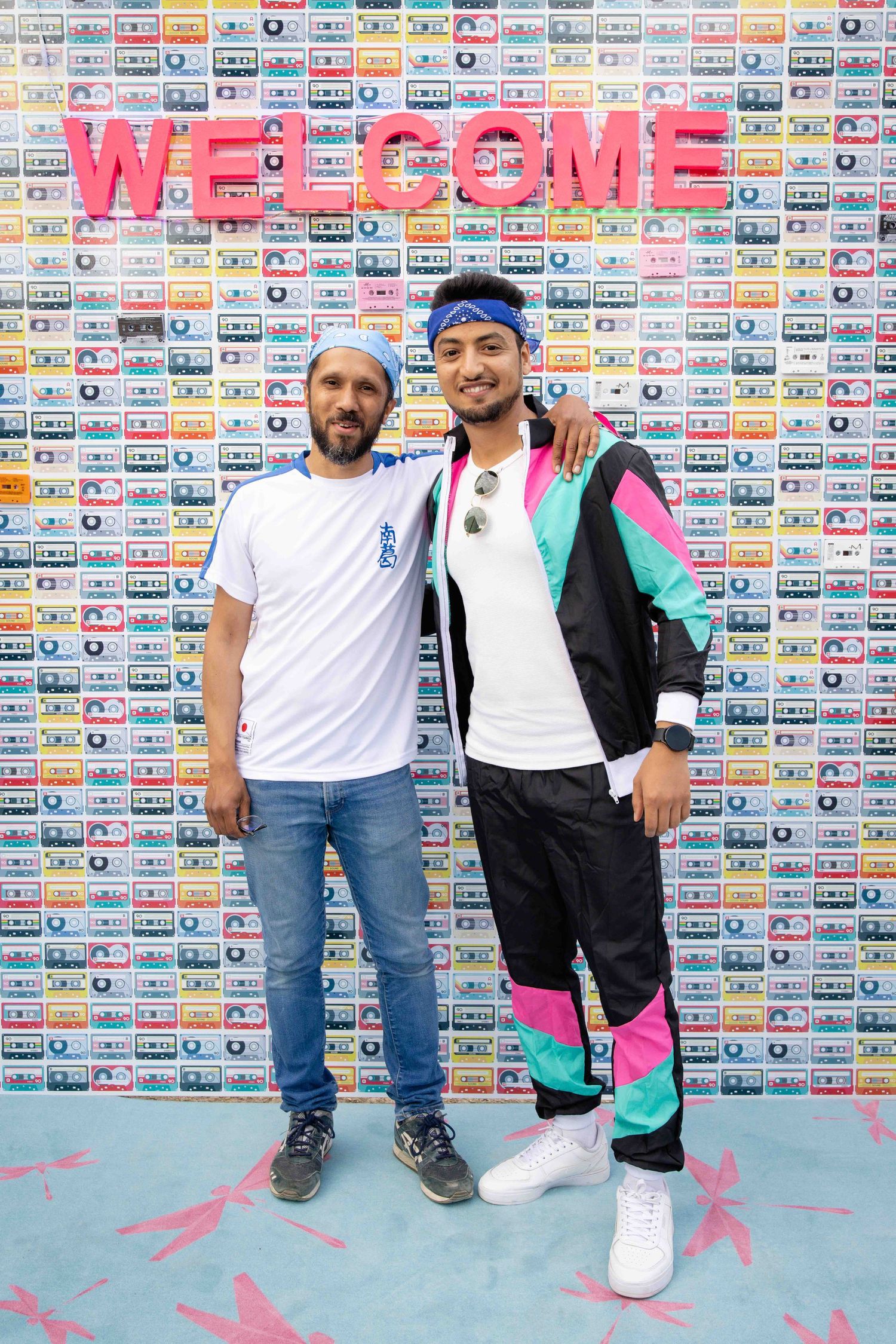 People in sporty white outfits and denim pose against wall decorated with vintage cassette tapes.
