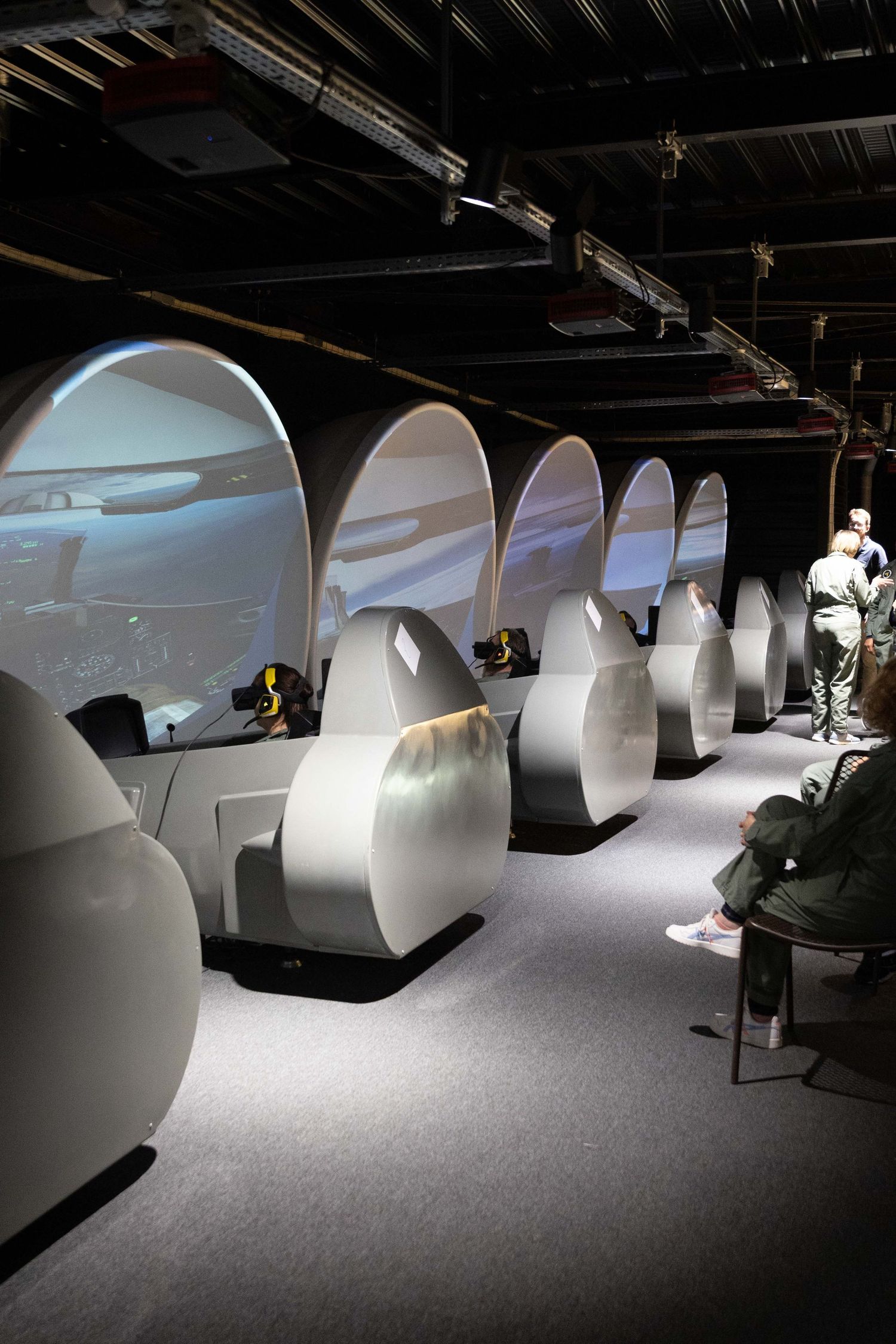 Row of white pod-shaped simulator stations in a dark room with dramatic lighting.