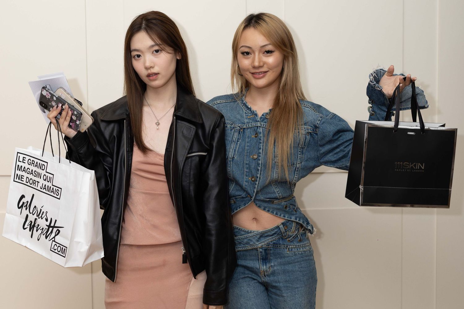 Two women holding shopping bags and smiling in white studio setting.