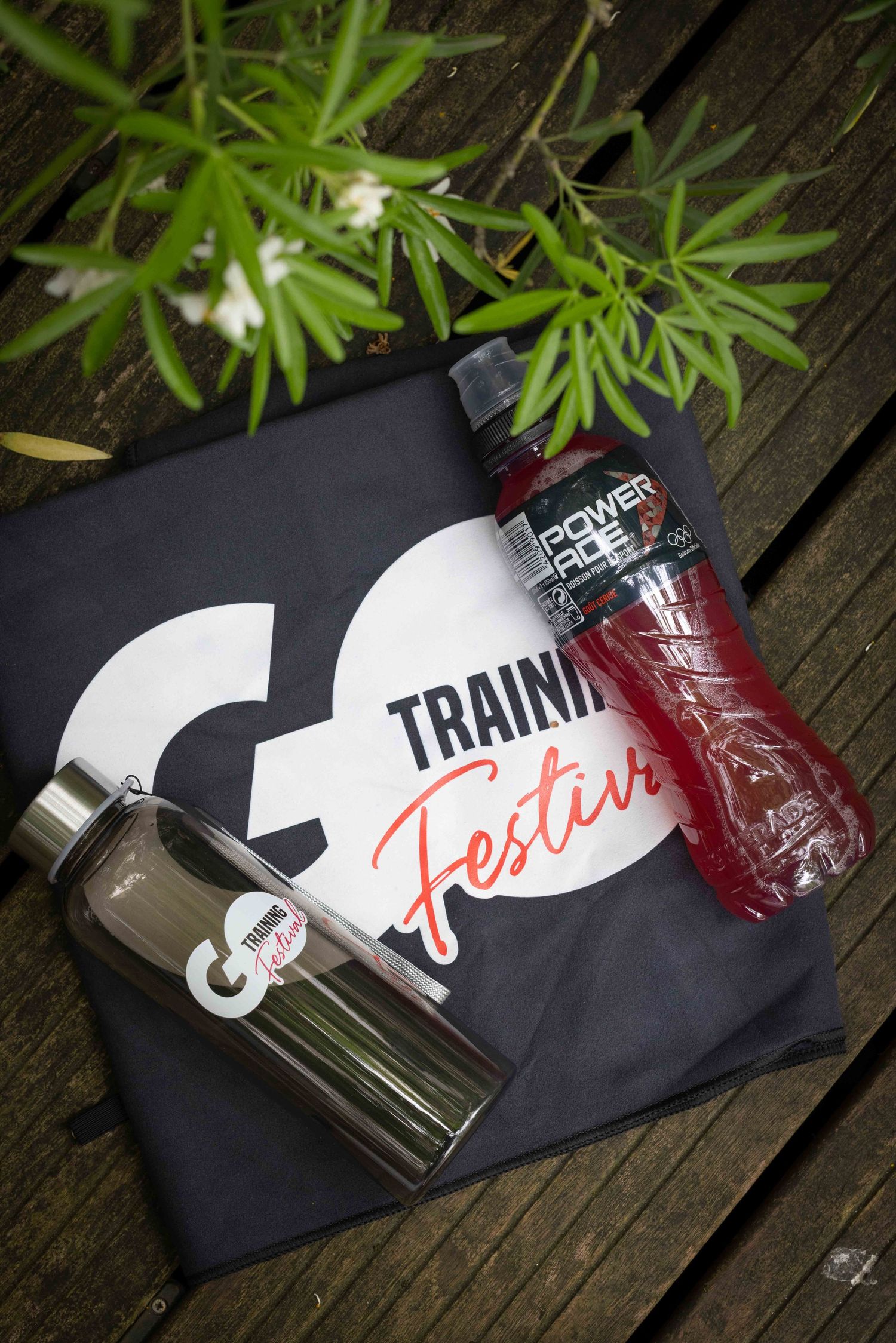 Branded fitness merchandise and water bottles displayed on wooden deck with green plants.