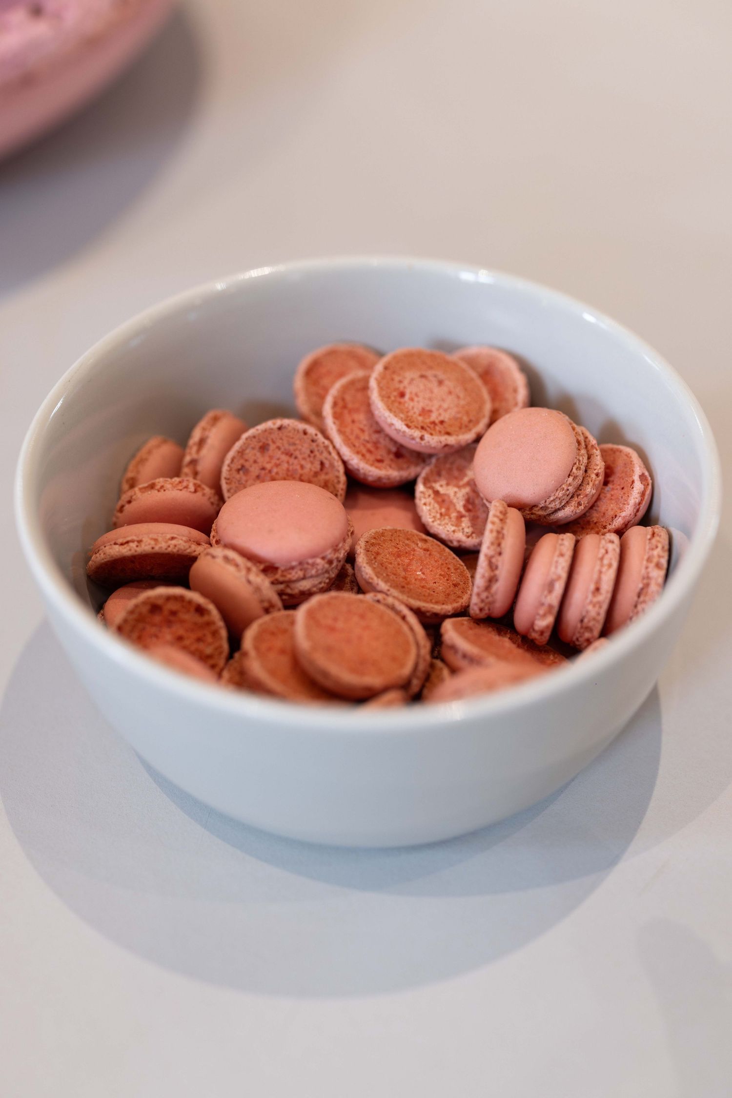 Bowl of pink macarons displayed on white surface.