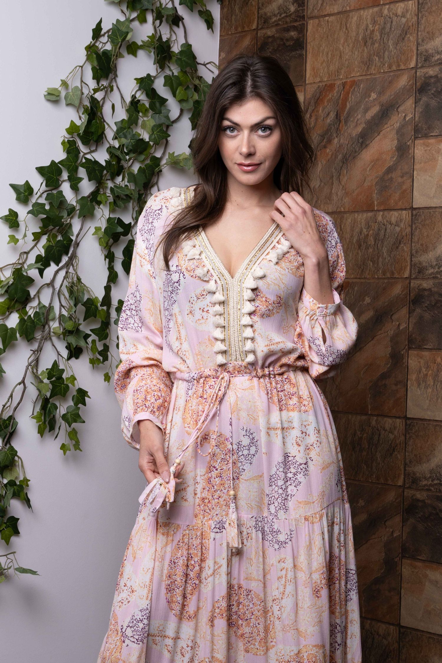 Robe longue bohème romantique à imprimé floral rose sur fond de mur en pierre.