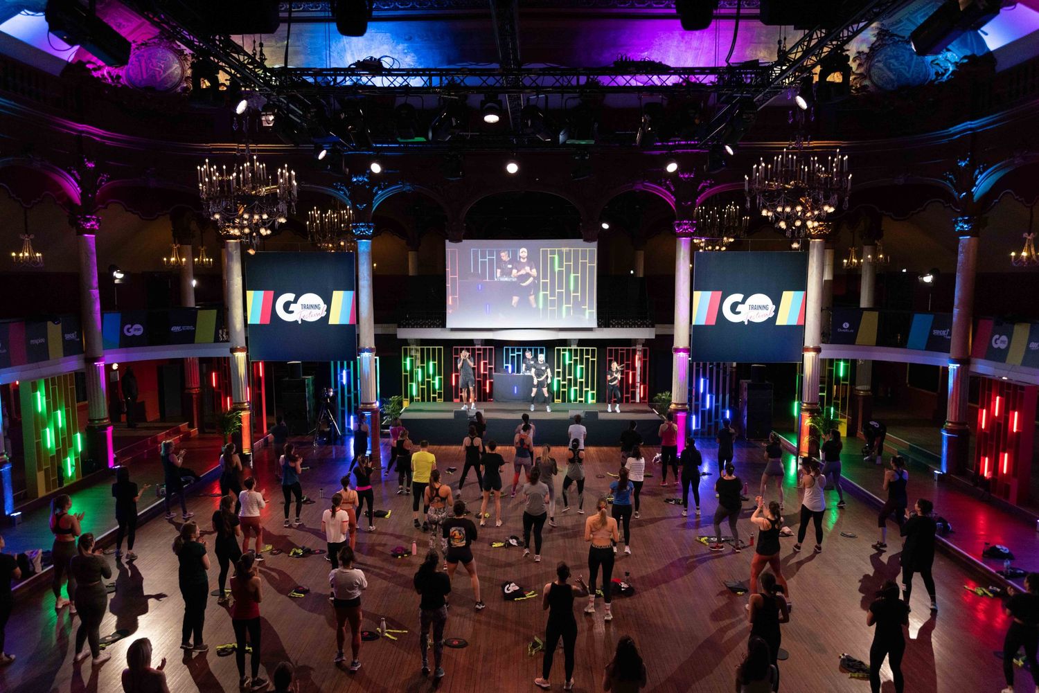 Panoramic view of a fitness class with multicolored lighting and participants spread across the room.
