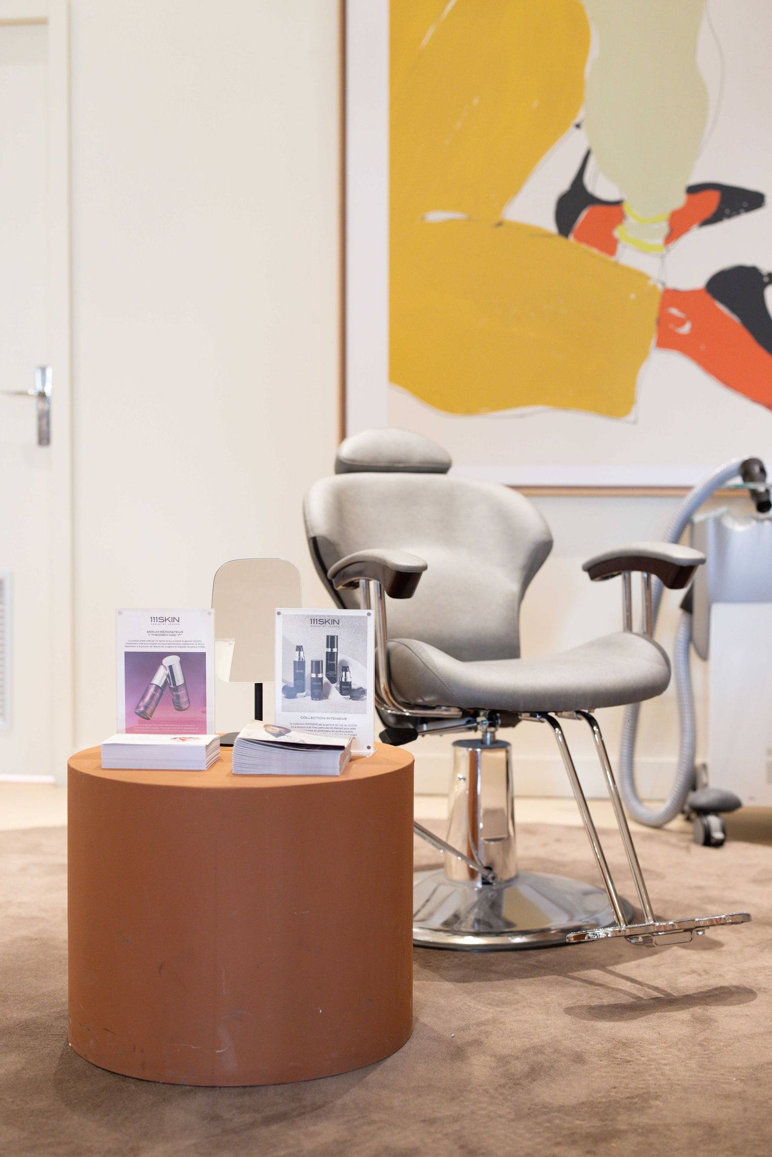 Modern office waiting area with gray chairs and round brown table against yellow wall art.
