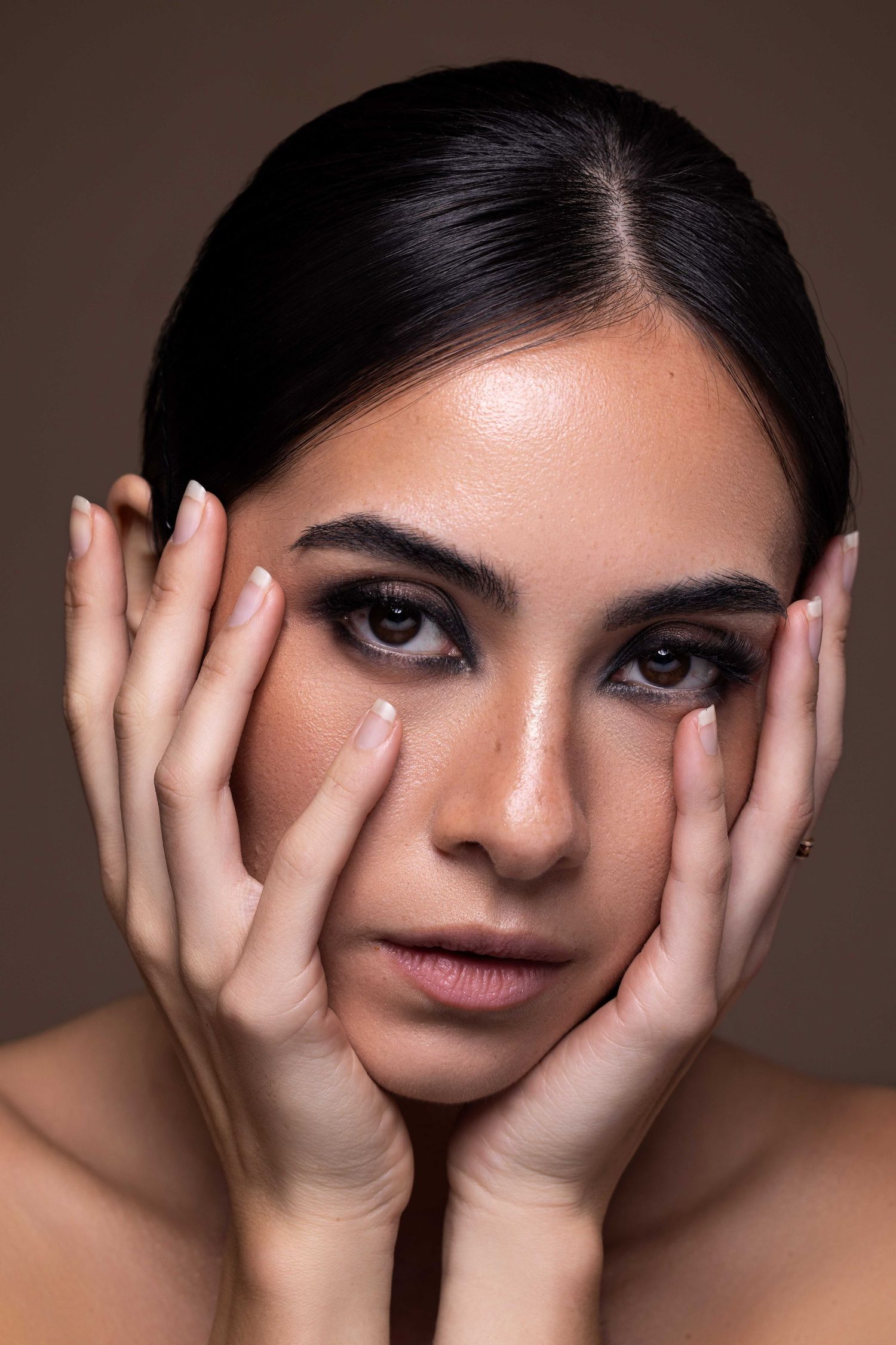 Portrait de beauté artistique avec les mains doucement posées sur les joues et un maquillage des yeux dramatique.