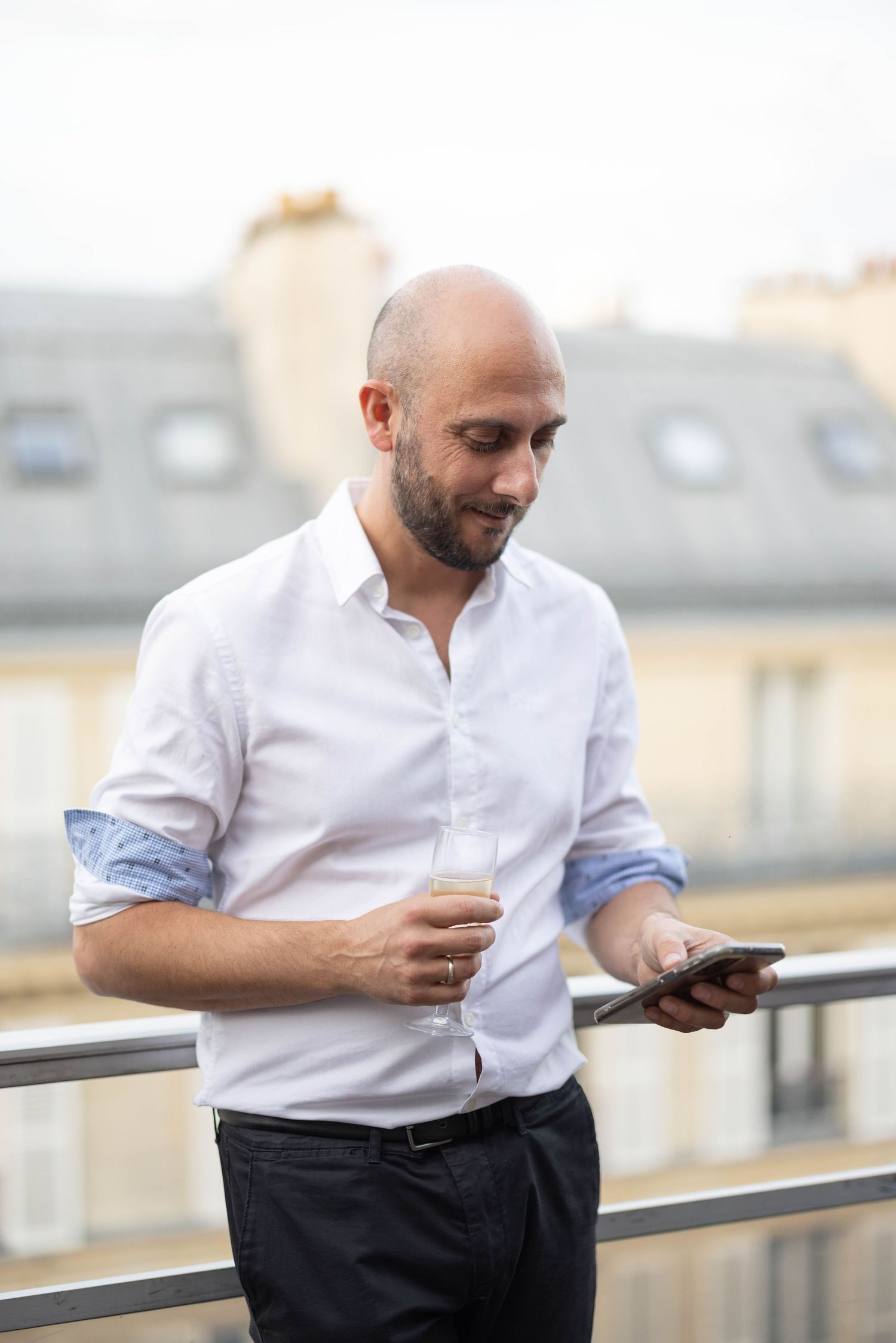 Person in white shirt checking phone on balcony with city rooftops in background.