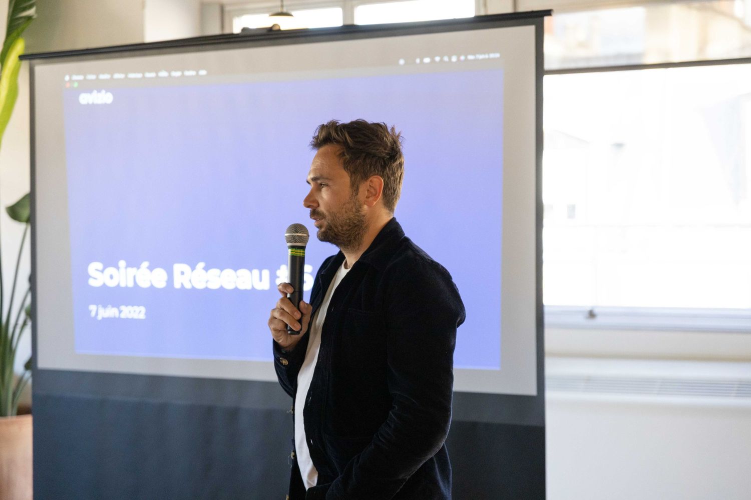A presenter speaking in front of a projection screen during a business presentation.