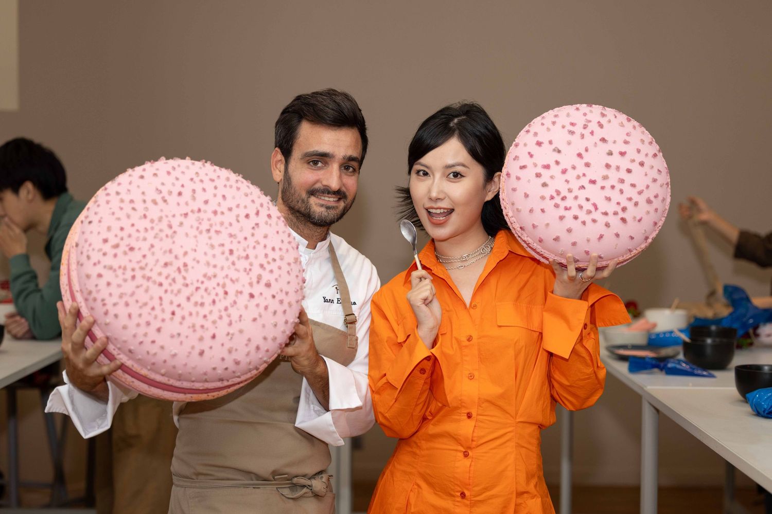 Des personnes en uniformes orange célèbrent avec des ballons roses lors d'un rassemblement en intérieur.