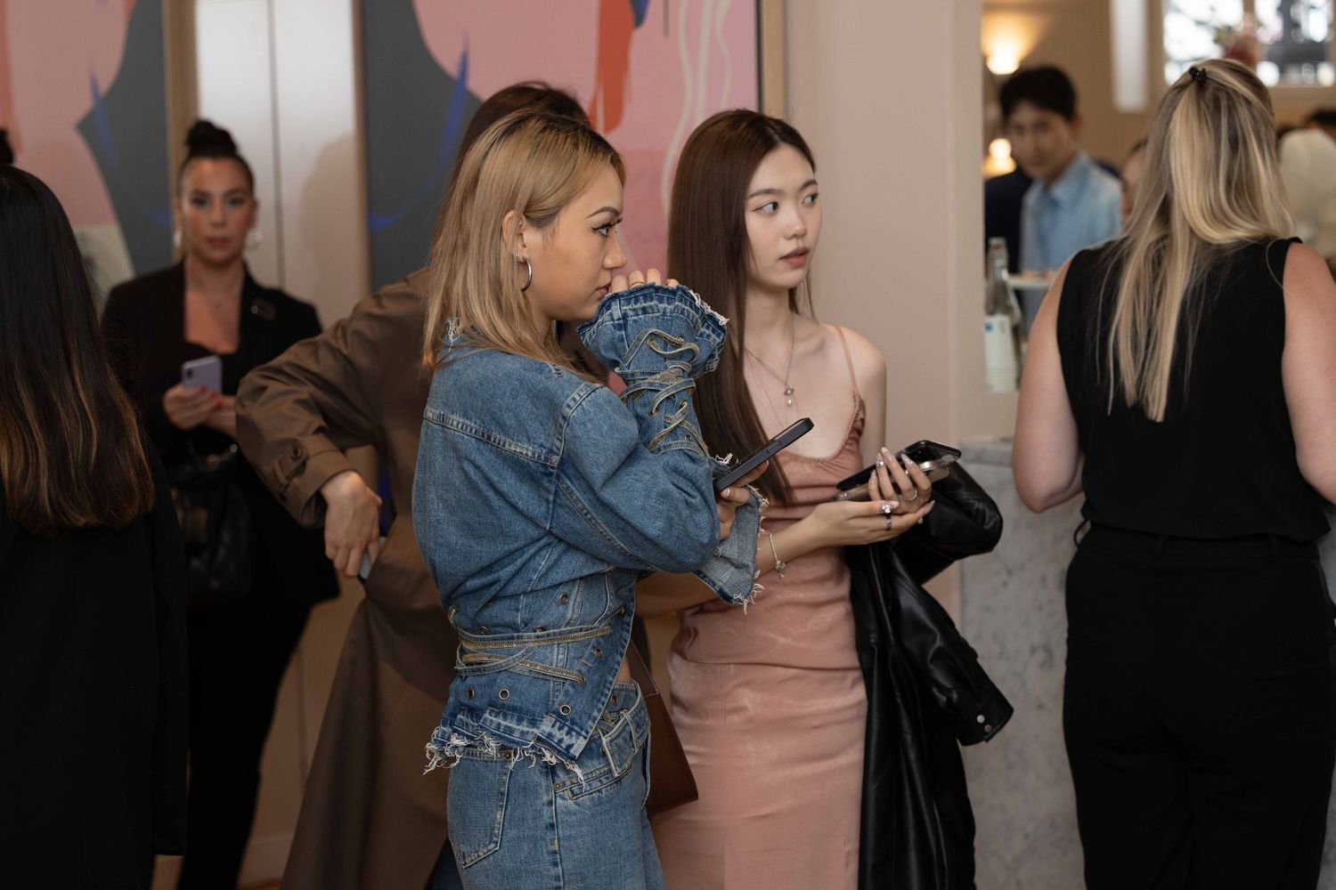 People mingling at an indoor event with pink and beige wall decor.