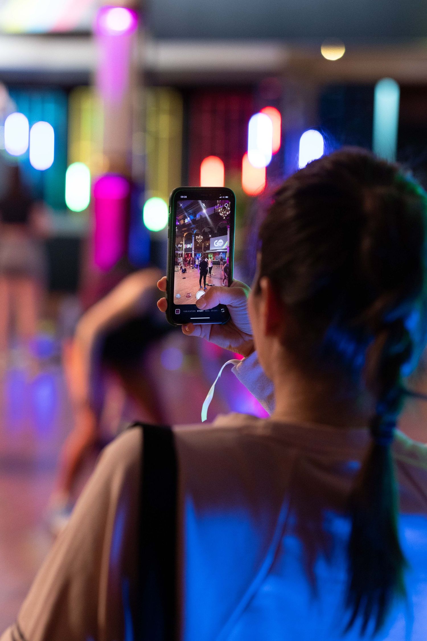 Person taking photo on smartphone in colorfully lit indoor venue space.