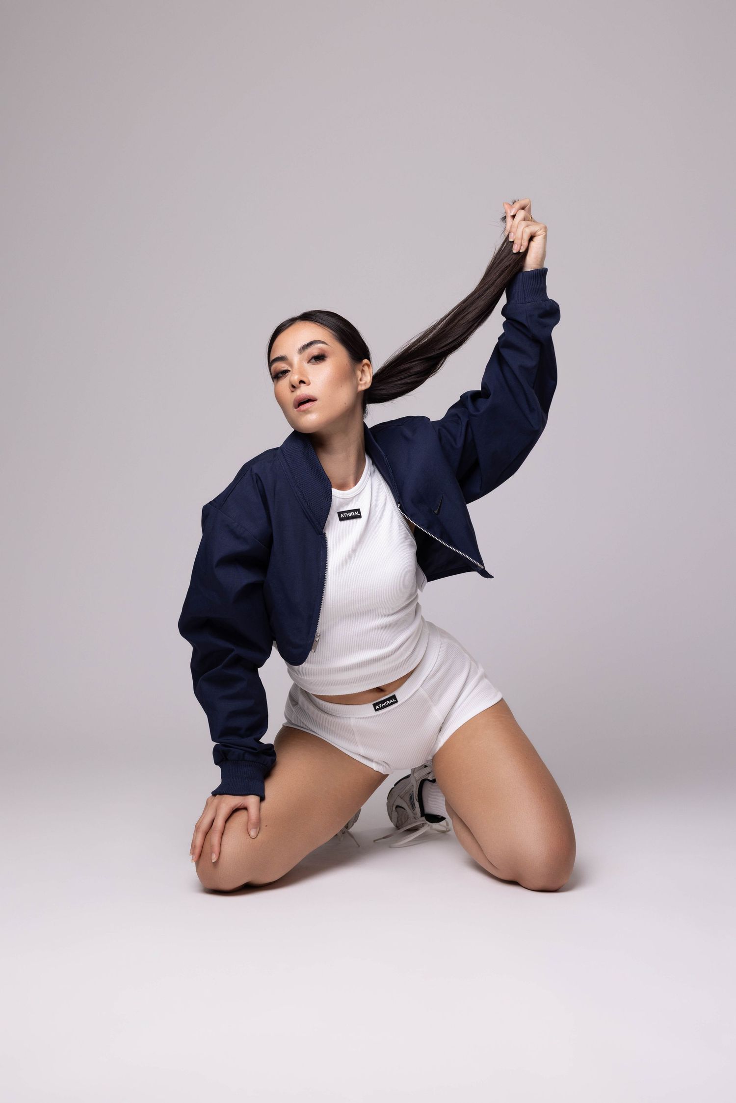 Modèle portant une veste bleu marine et un ensemble de vêtements de sport blancs pose avec de longs cheveux noirs.