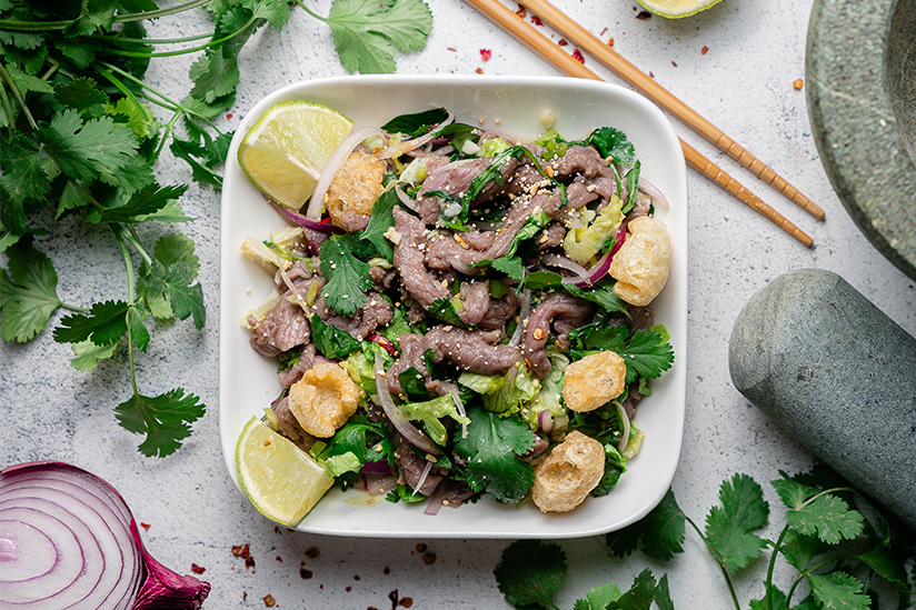 Asian cuisine dish with fresh herbs, lime wedges and chopsticks styled for food photography.