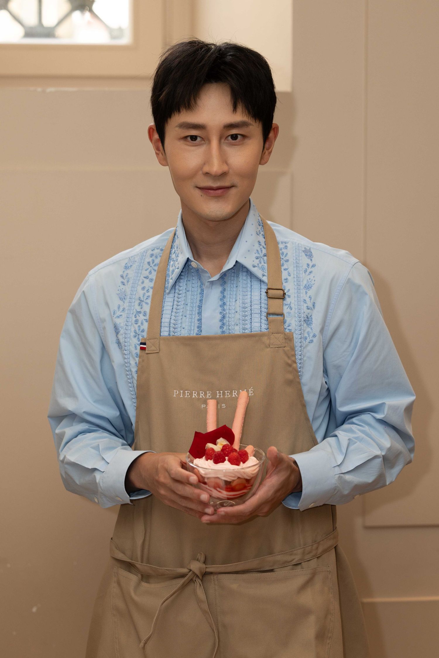 Person wearing a tan apron and blue shirt presenting a decorated dessert.