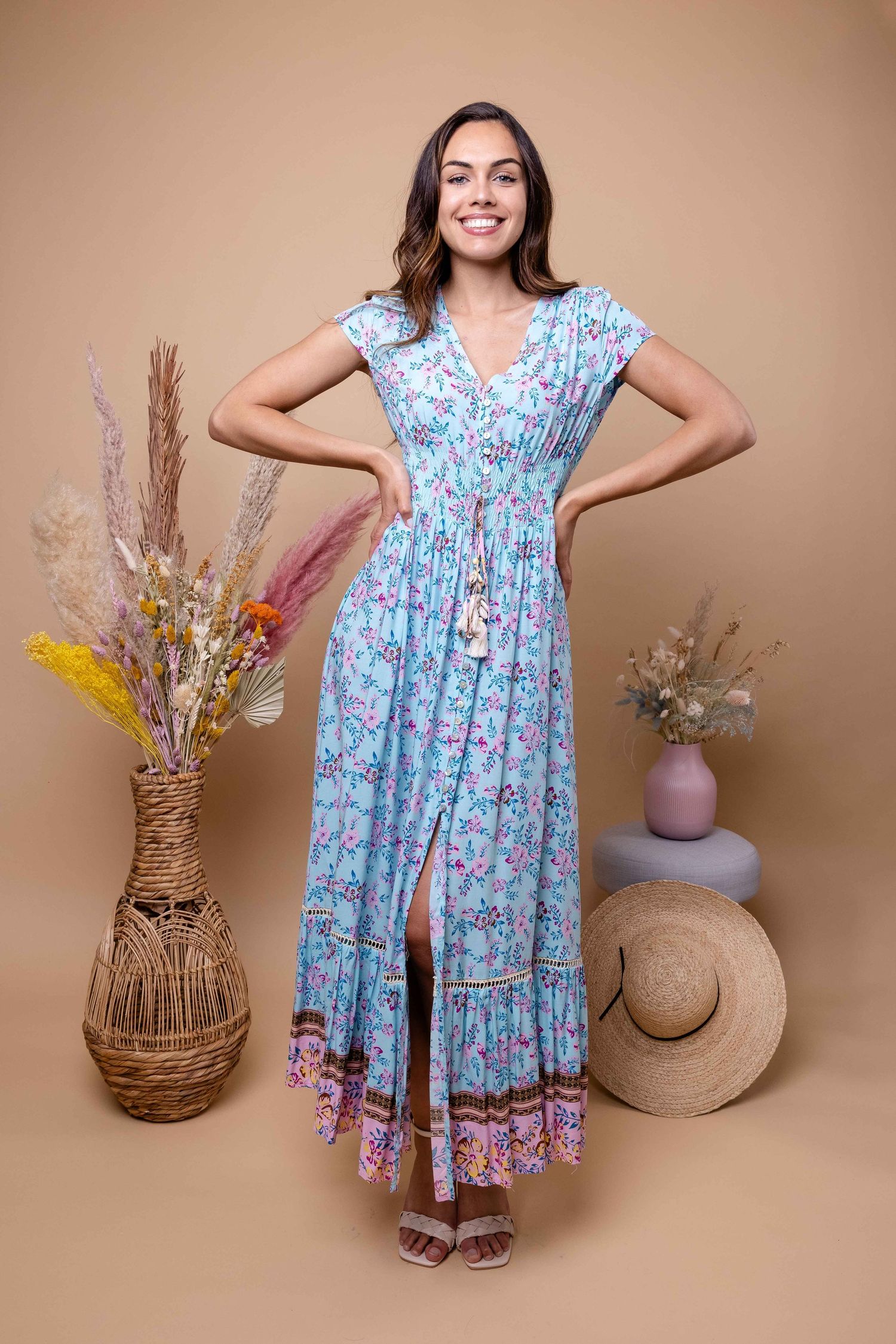 Le mannequin en robe fleurie bleu clair virevolte près de paniers tressés et de fleurs séchées.