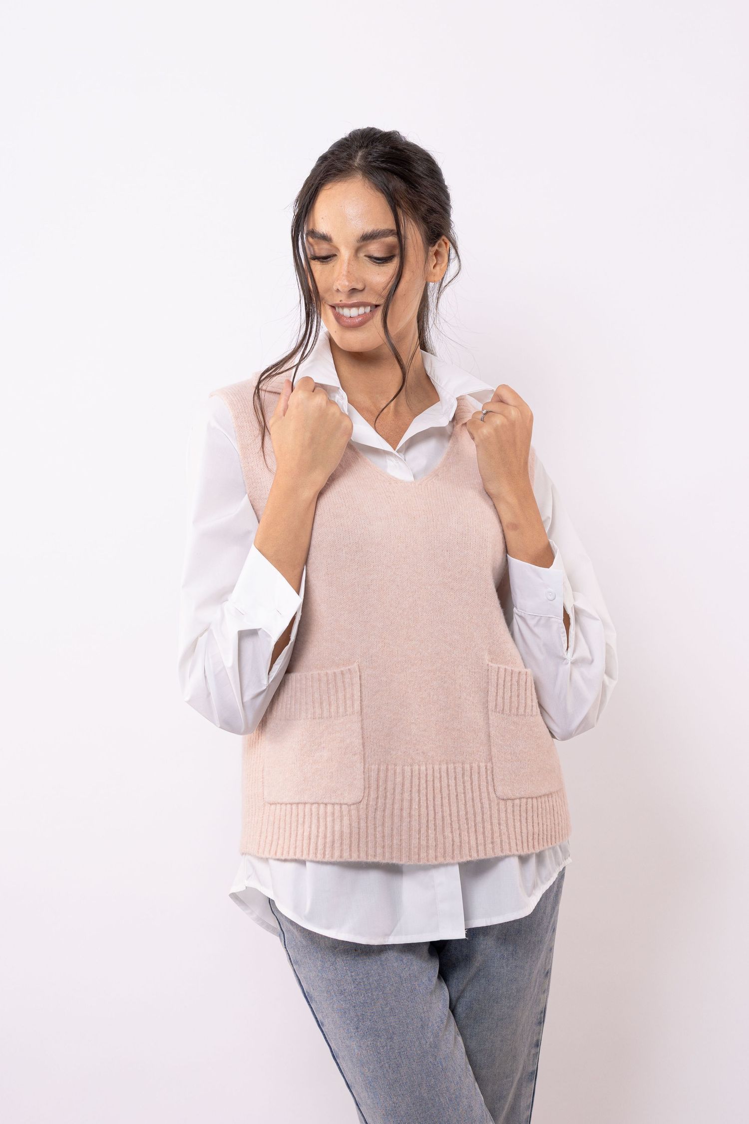 Gilet en tricot rose superposé sur une chemise blanche boutonnée avec un jean.