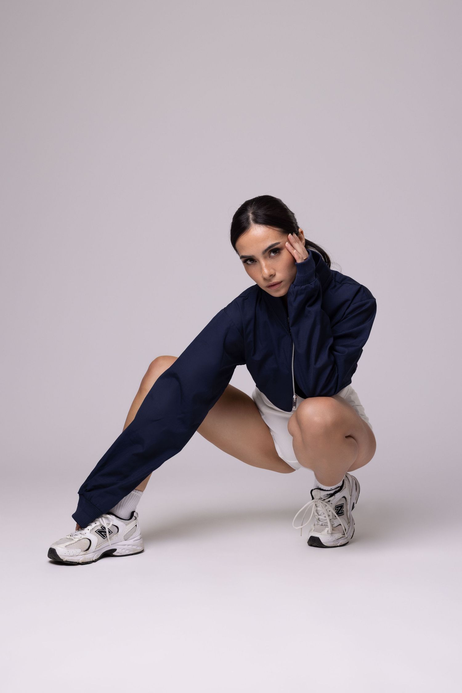 Pose sportive en survêtement bleu marine et crop top blanc avec des baskets de sport.