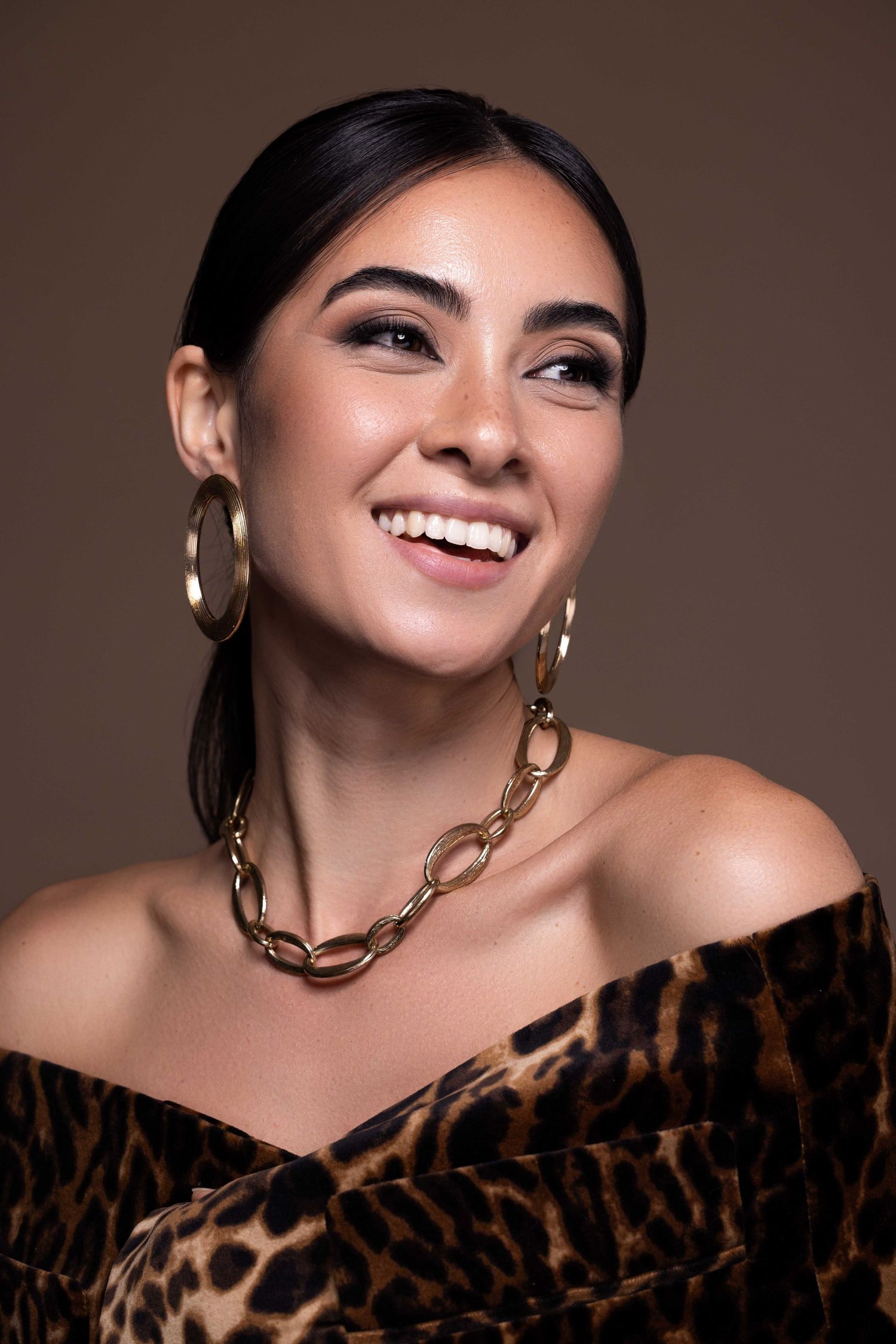 Portrait de mode joyeux en haut imprimé léopard avec bijoux en or et sourire radieux.