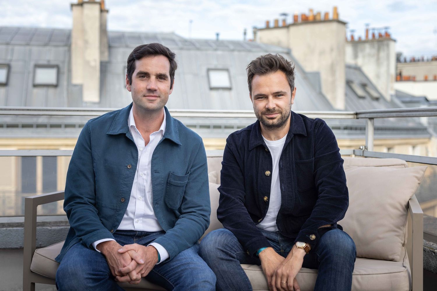 Two people relaxing on outdoor furniture with Parisian rooftops in background.
