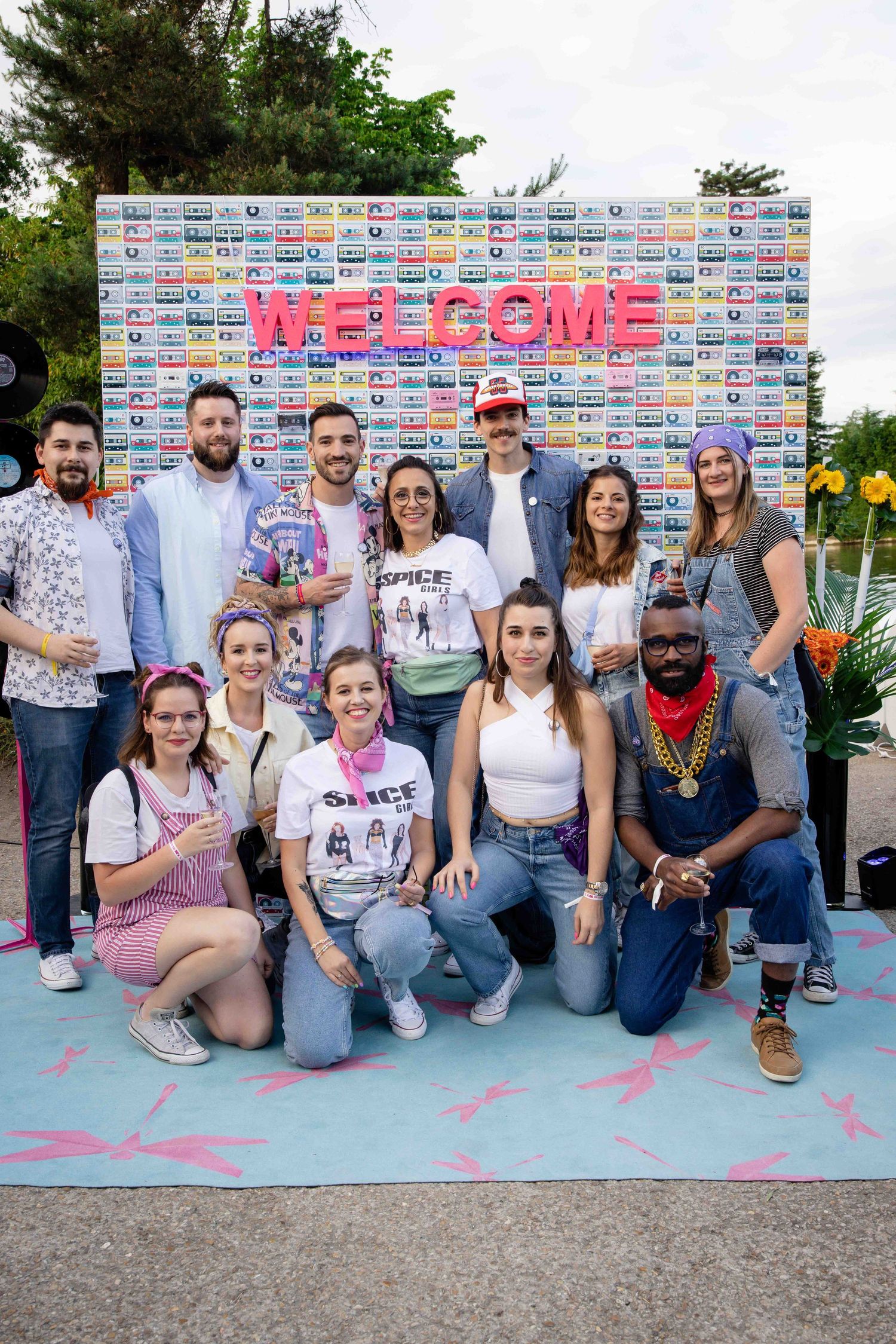 Group photo of people gathered in front of a decorative welcome wall with vintage cassette tape design.