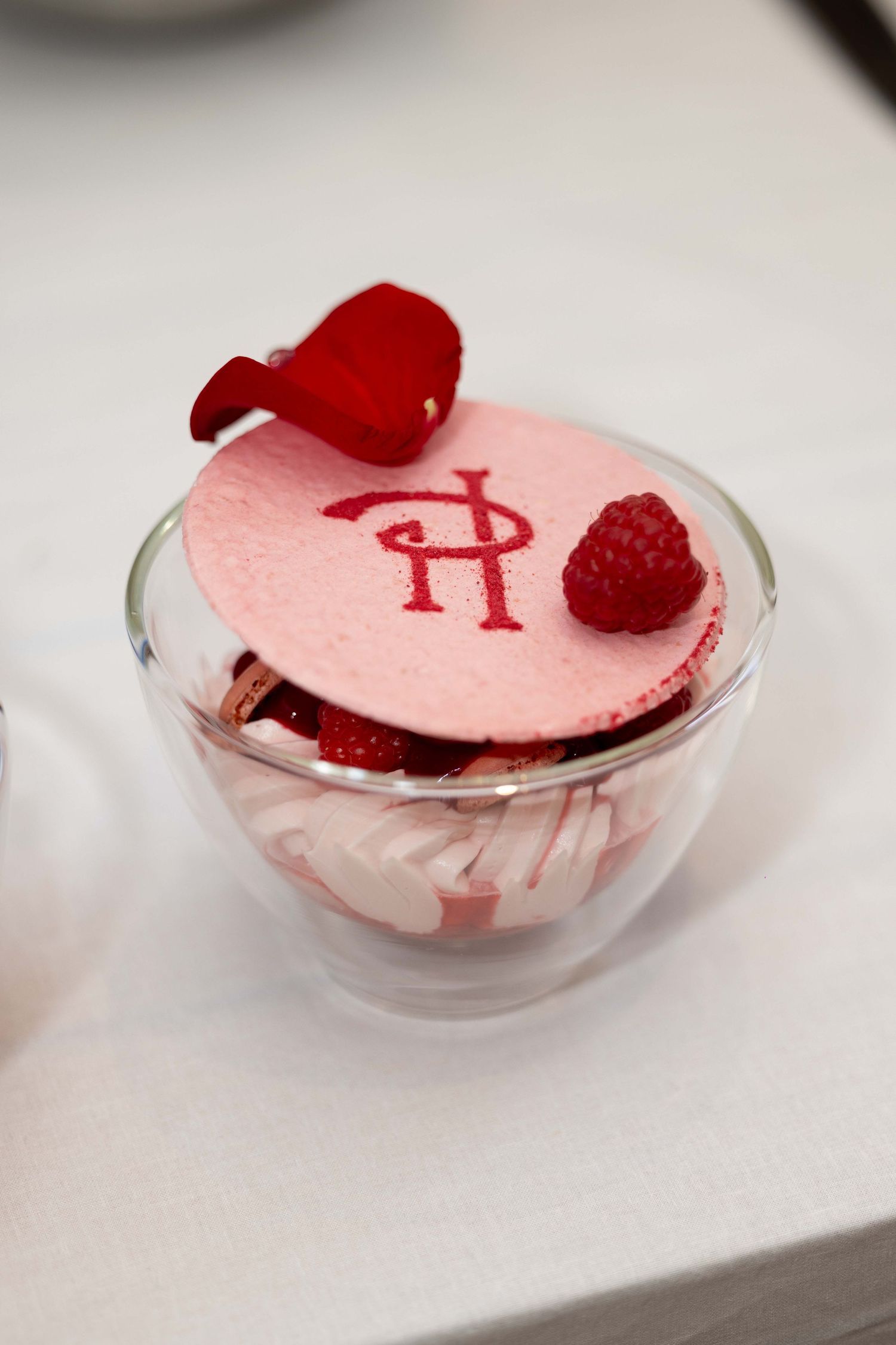 Pink dessert with red raspberries served in a clear glass bowl on white surface.