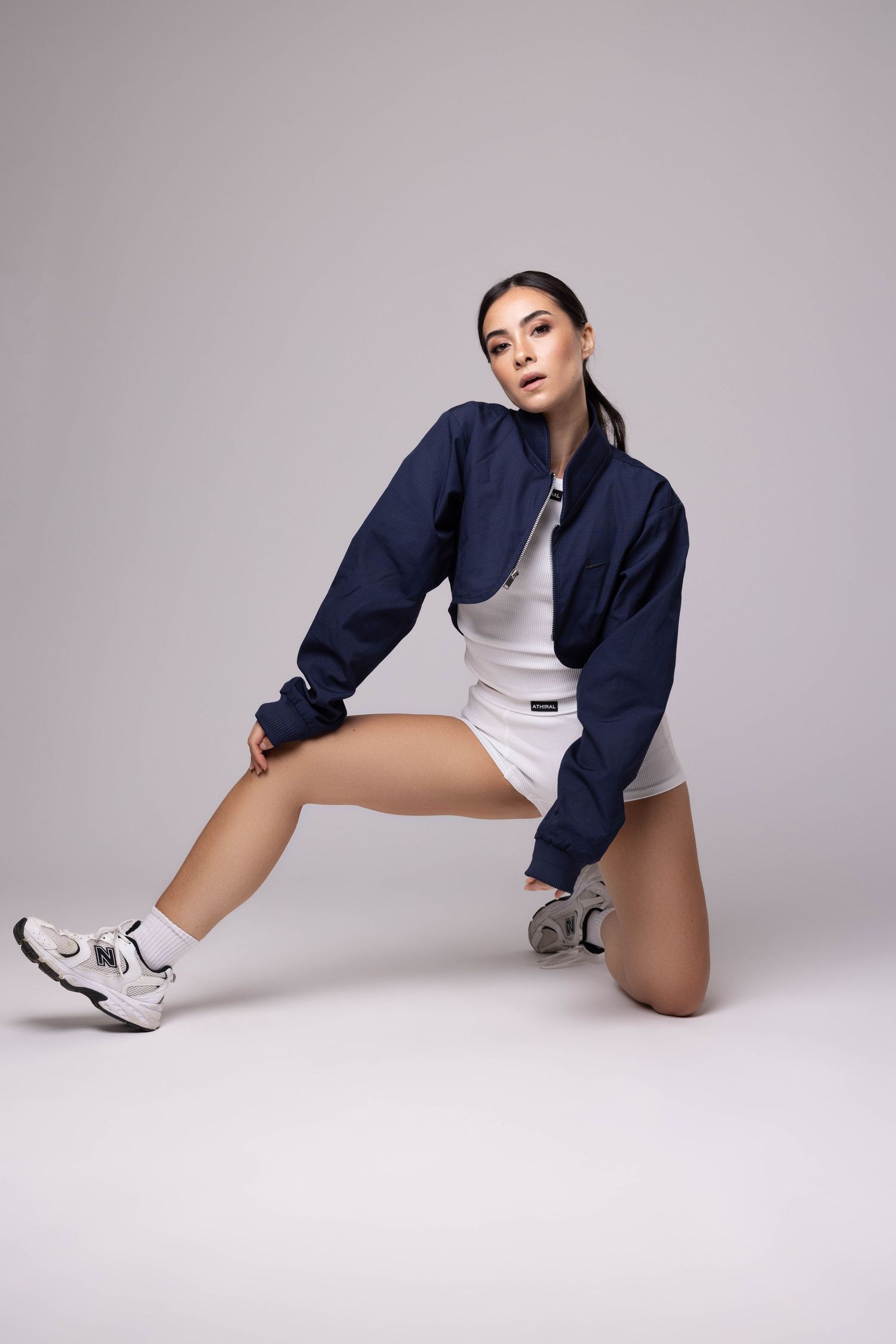 Pose athlétique en veste bleu marine et short blanc sur fond neutre.