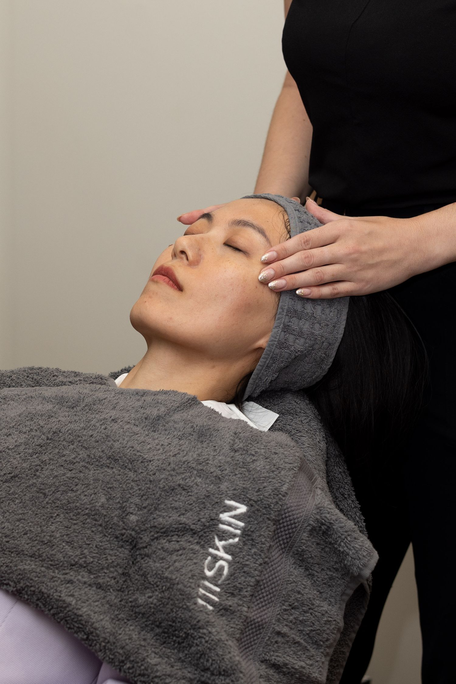 Woman receiving relaxing facial massage treatment on grey towel at luxury spa.