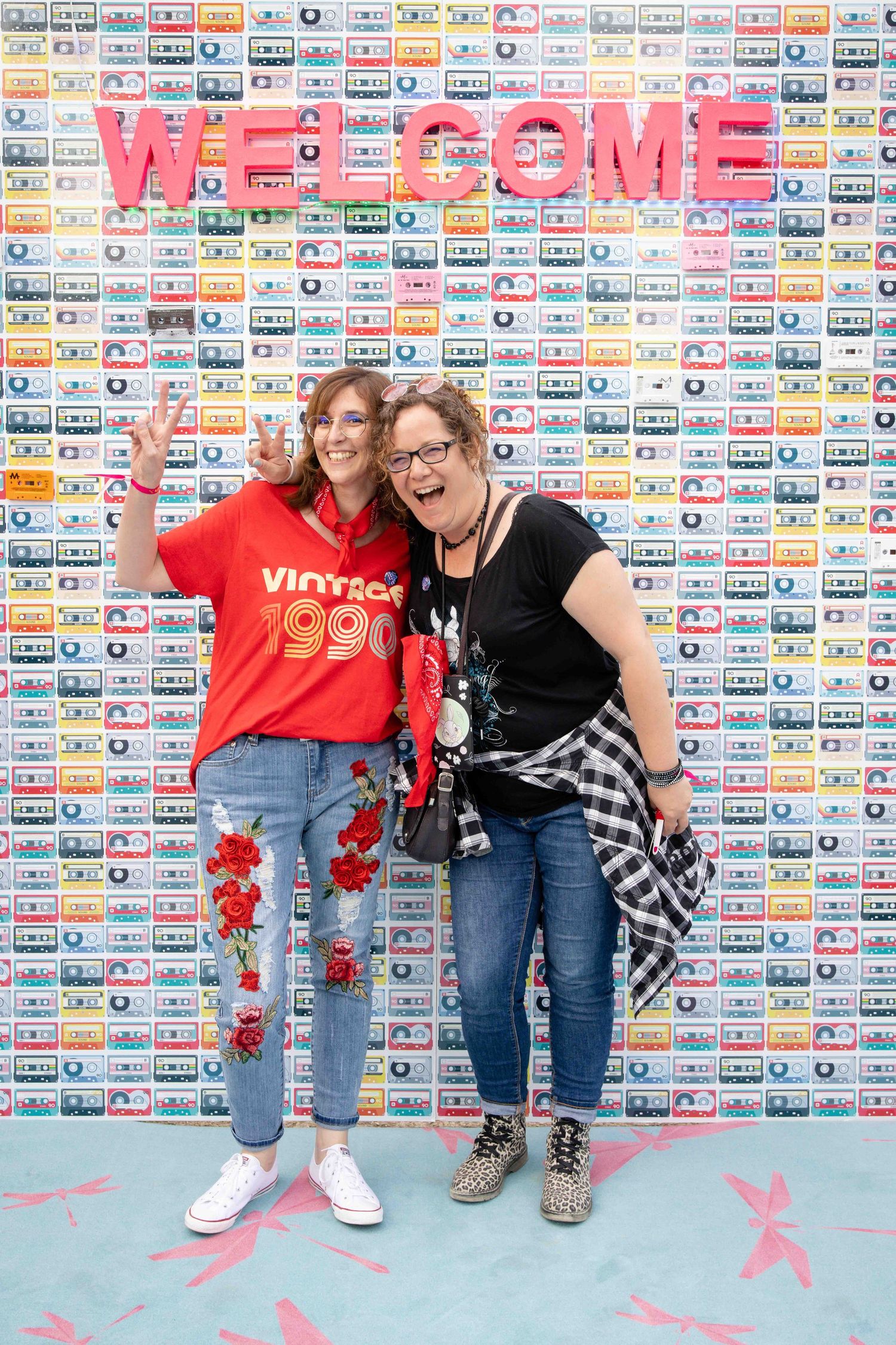 Friends in casual denim outfits pose together against wall covered in vintage cassette tape artwork.