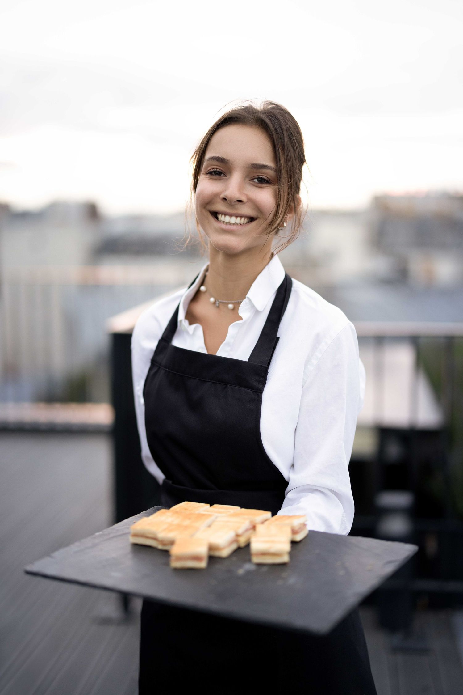 Server holding a tray of sandwiches on a rooftop terrace.