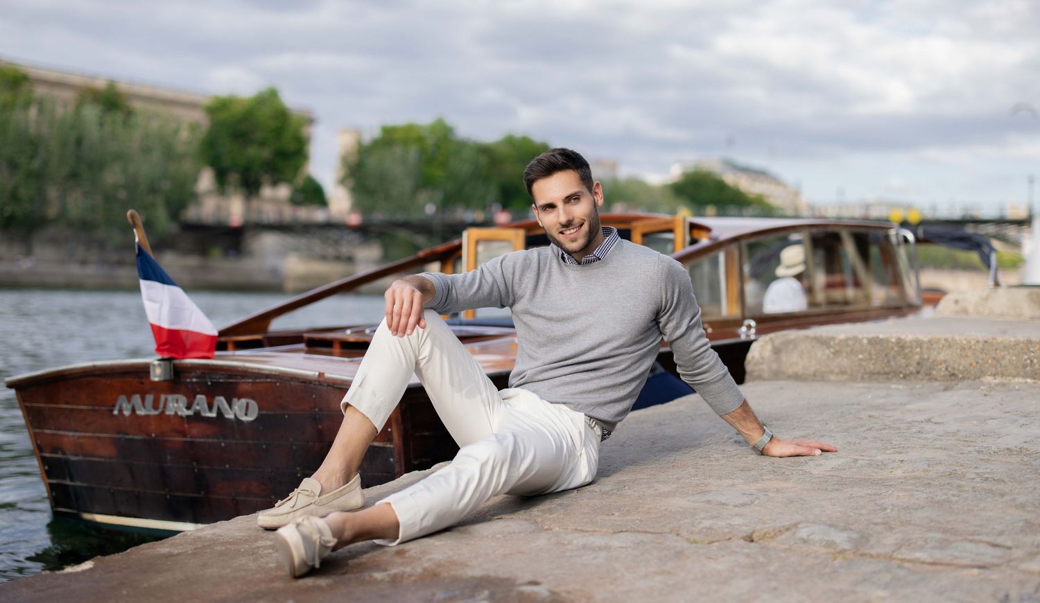 Homme en tenue décontractée allongé sur une surface en pierre près de l'eau et des bateaux.