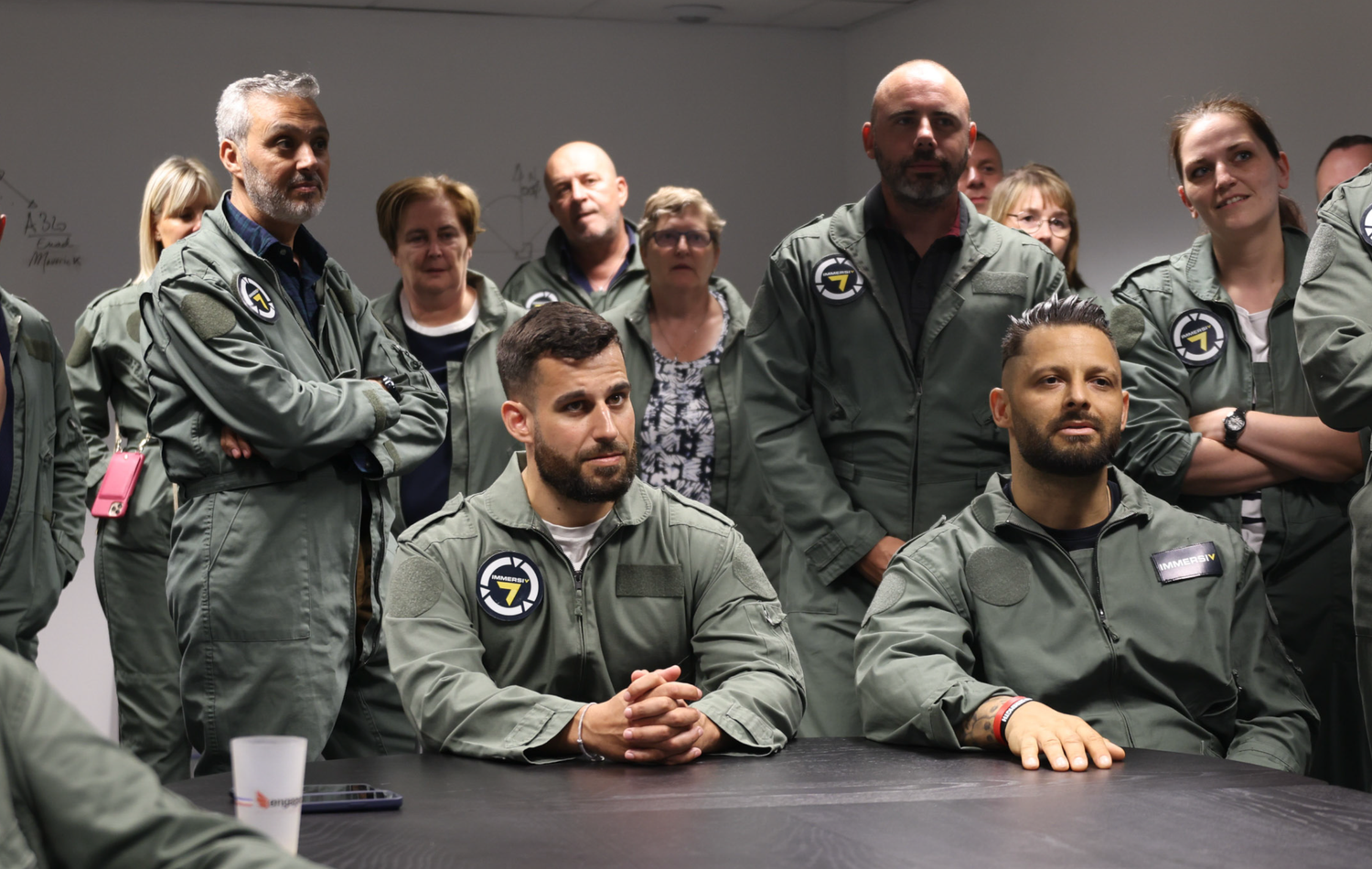 Group meeting scene with people seated at tables wearing matching gray uniforms.