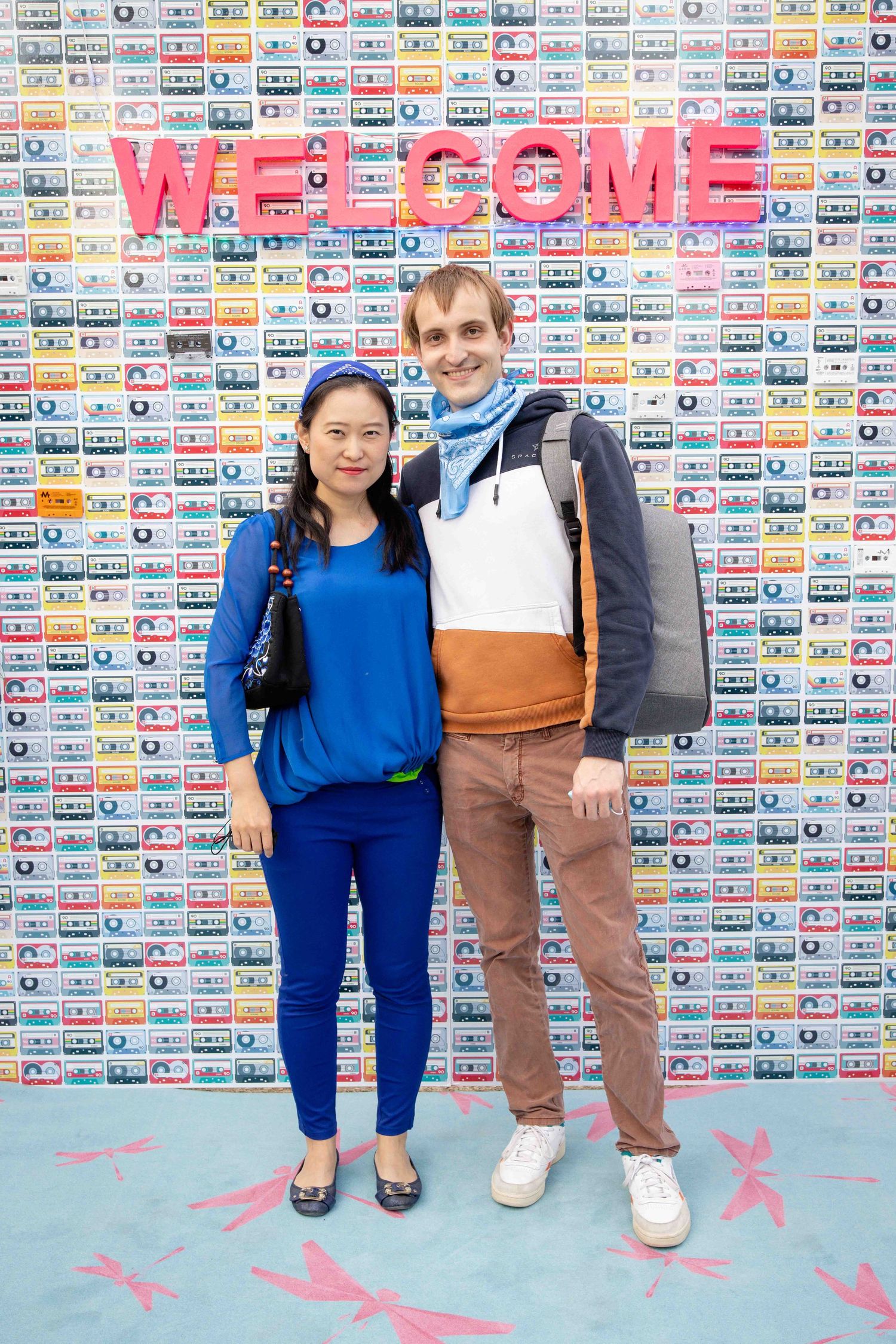 People in coordinated blue and brown outfits stand in front of wall decorated with cassette tape pattern.