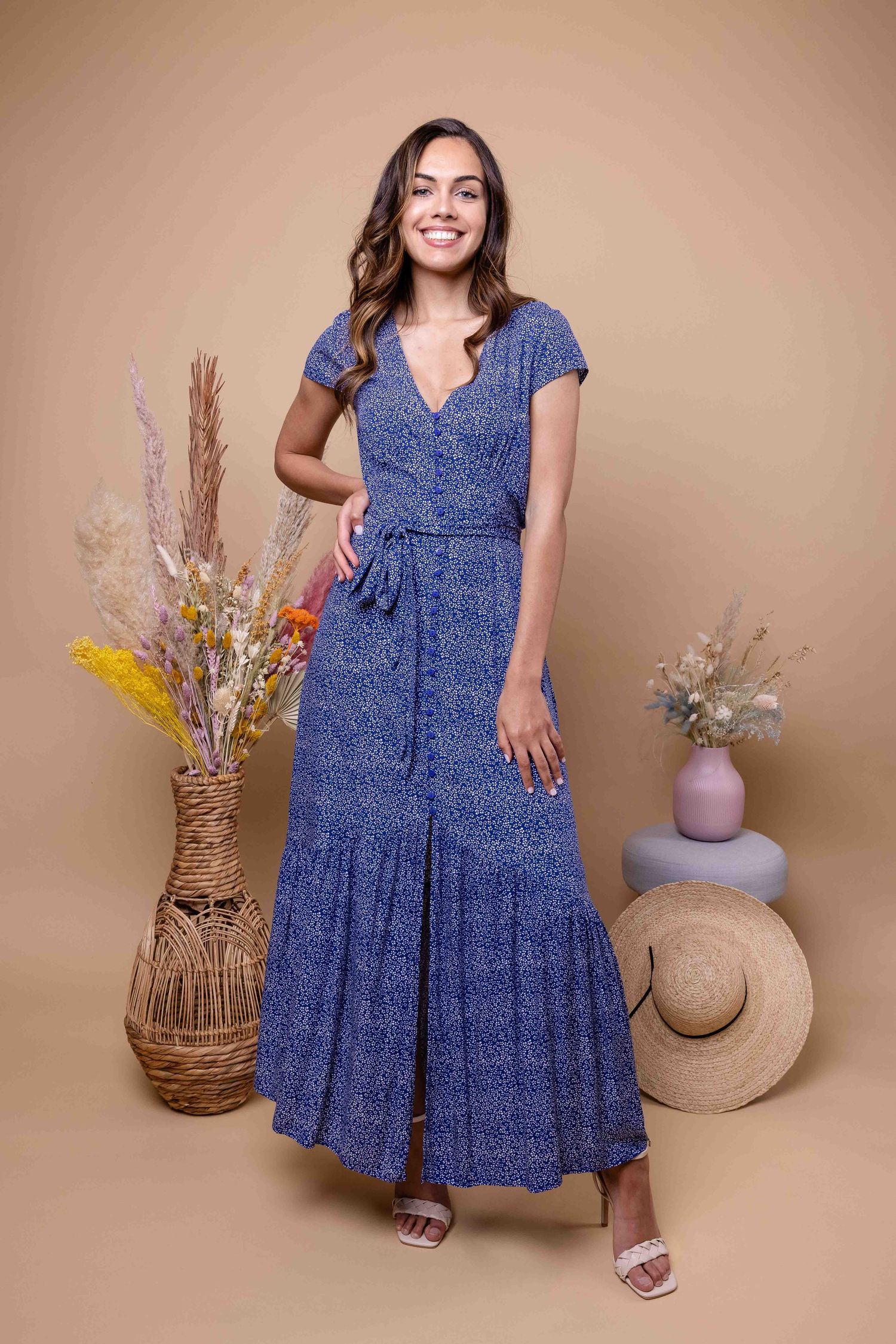 Le mannequin en robe à volants bleu marine pose avec des paniers tressés et des fleurs séchées.