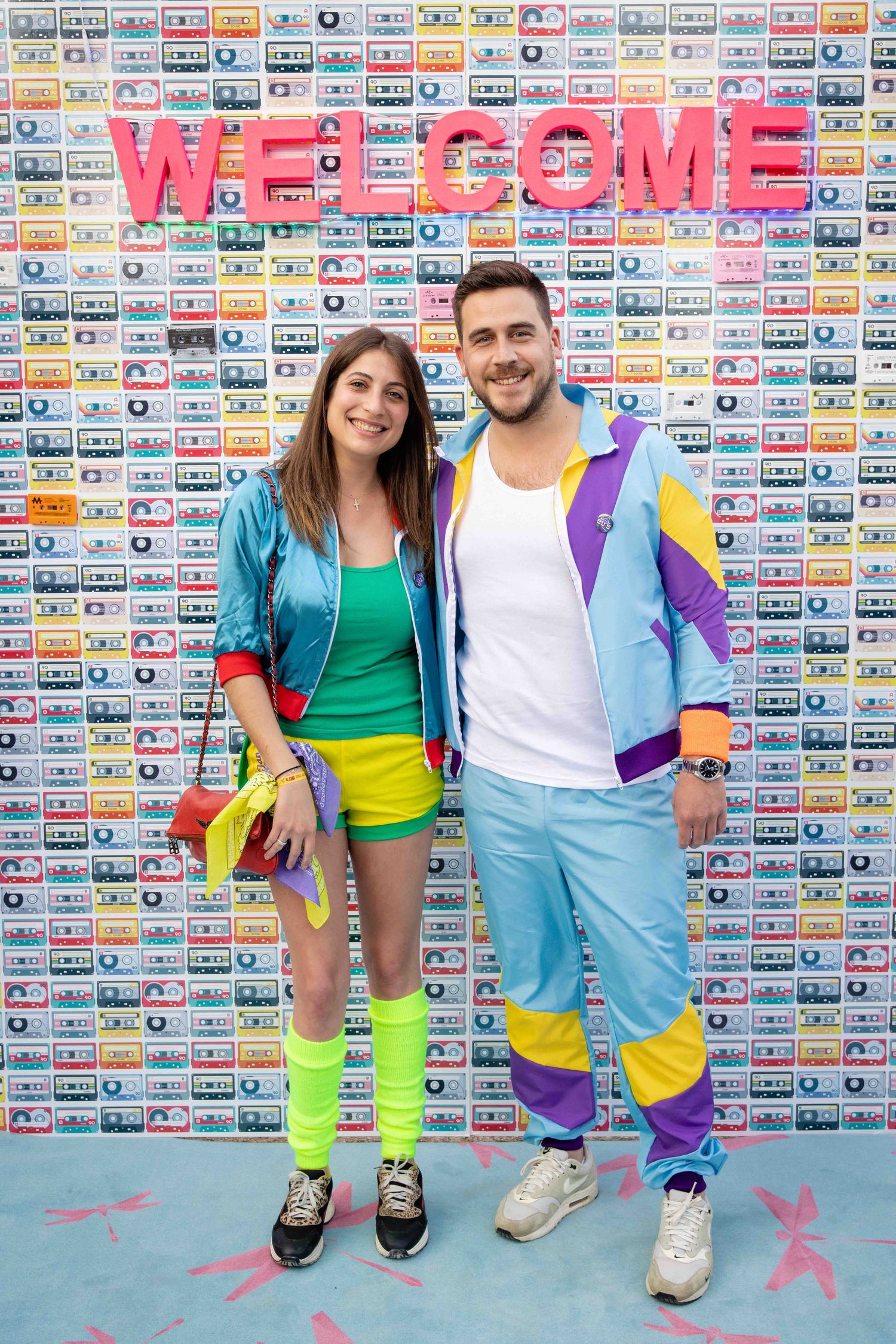 Group in colorful athletic wear poses against wall decorated with retro cassette tape pattern.