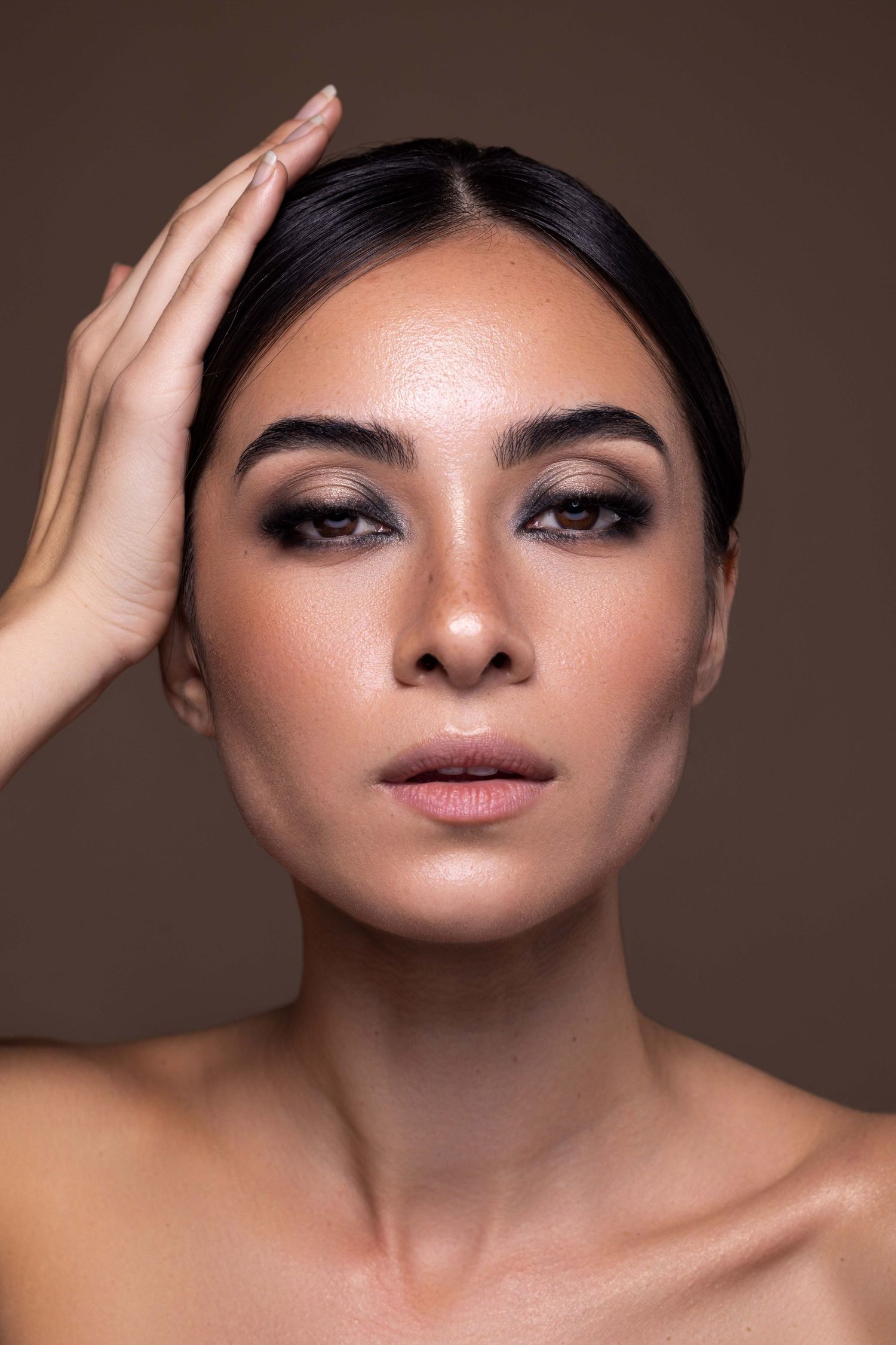 Portrait de beauté professionnel avec un éclairage dramatique et une peau éclatante sur fond marron foncé.