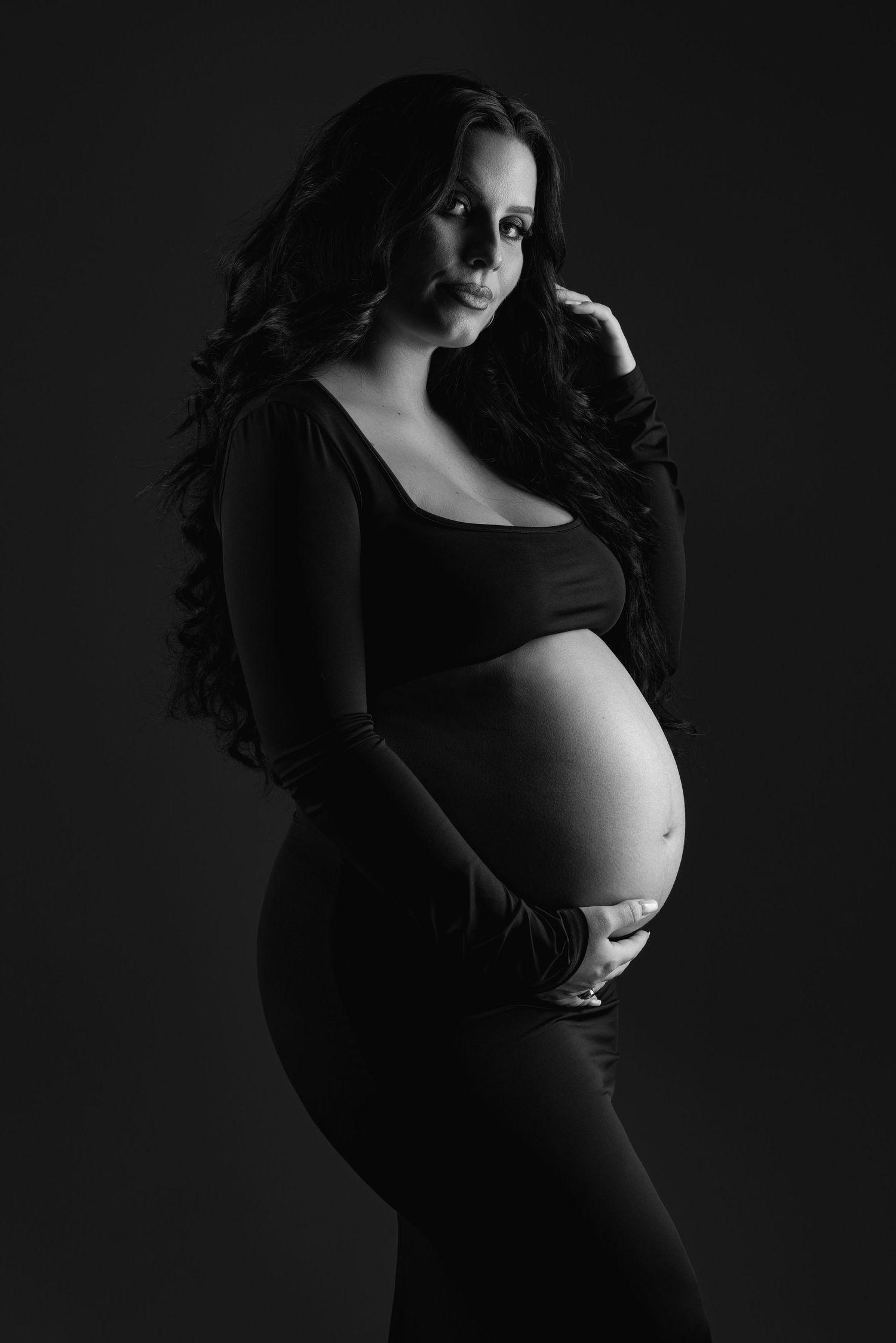 Dramatic black and white maternity photography series showing silhouette of pregnant woman in dark lighting.