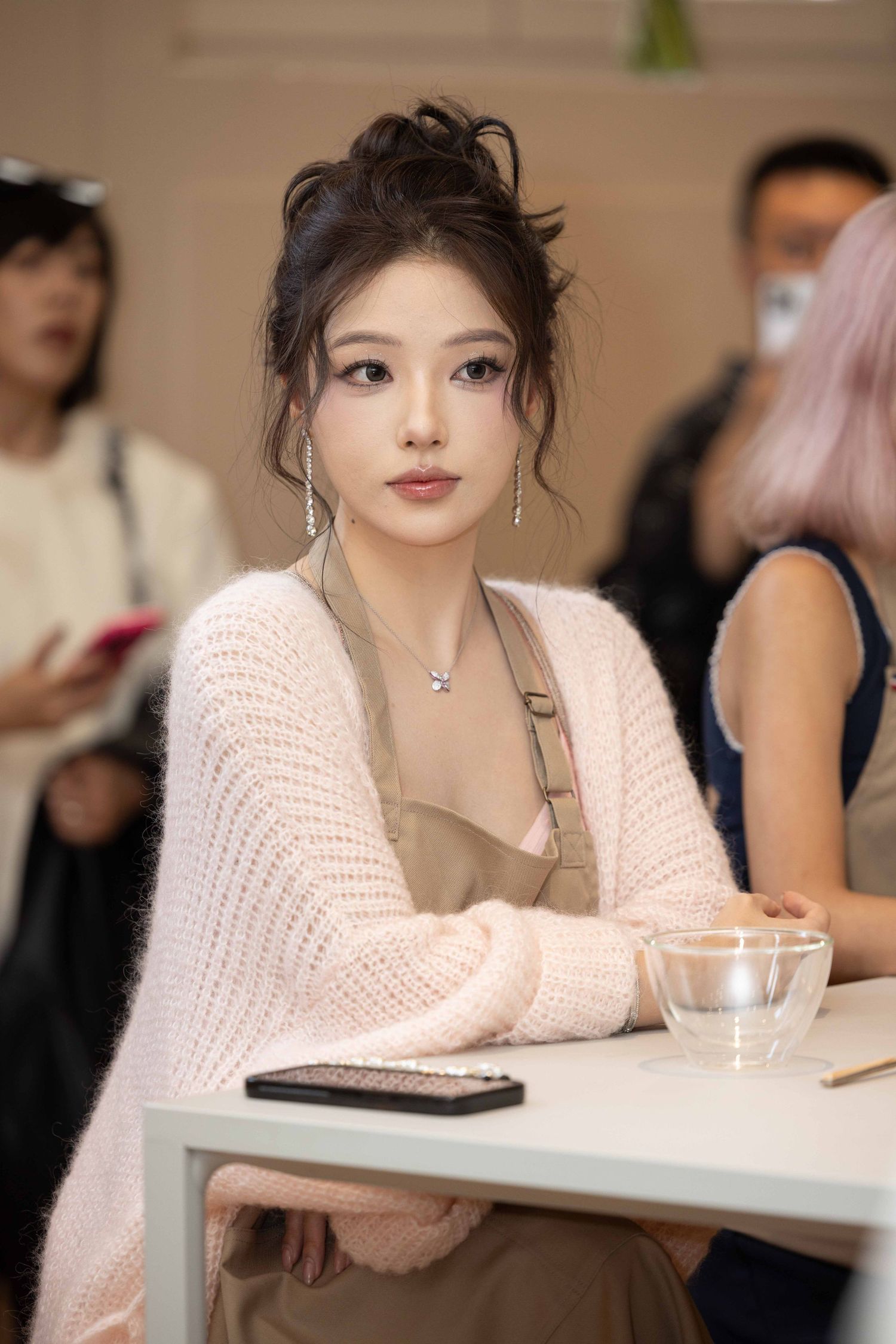 Person in soft pink sweater resting at white table during indoor event.