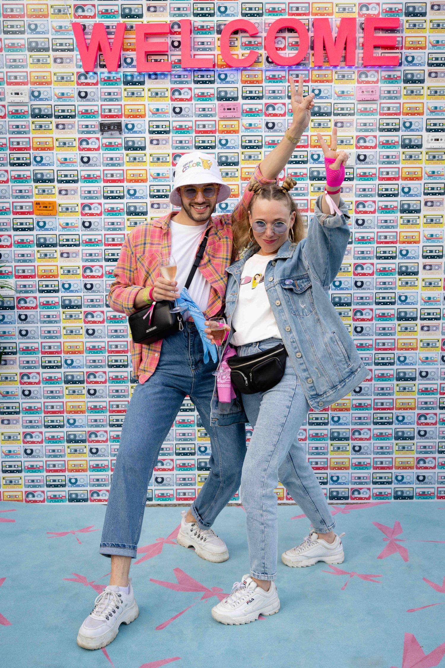 Group in denim and jean jackets strike energetic poses against wall of colorful cassette tapes.