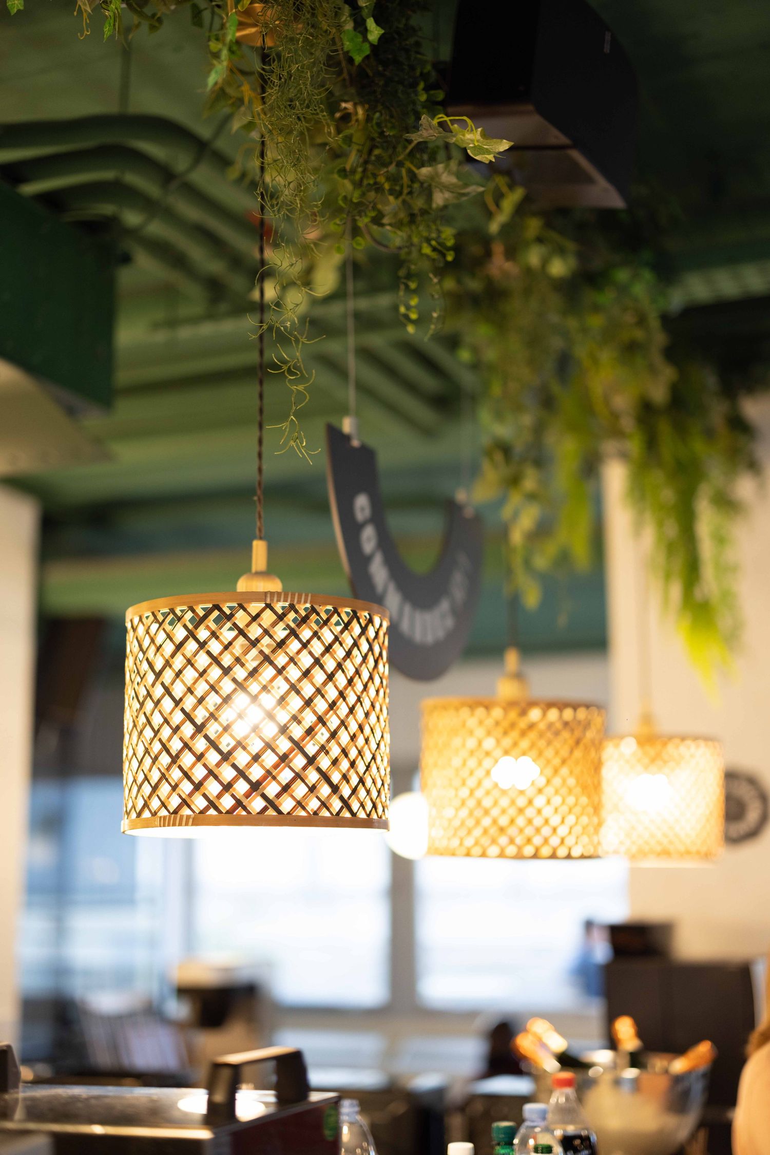 Decorative woven pendant lights hanging from ceiling with greenery in a restaurant setting.